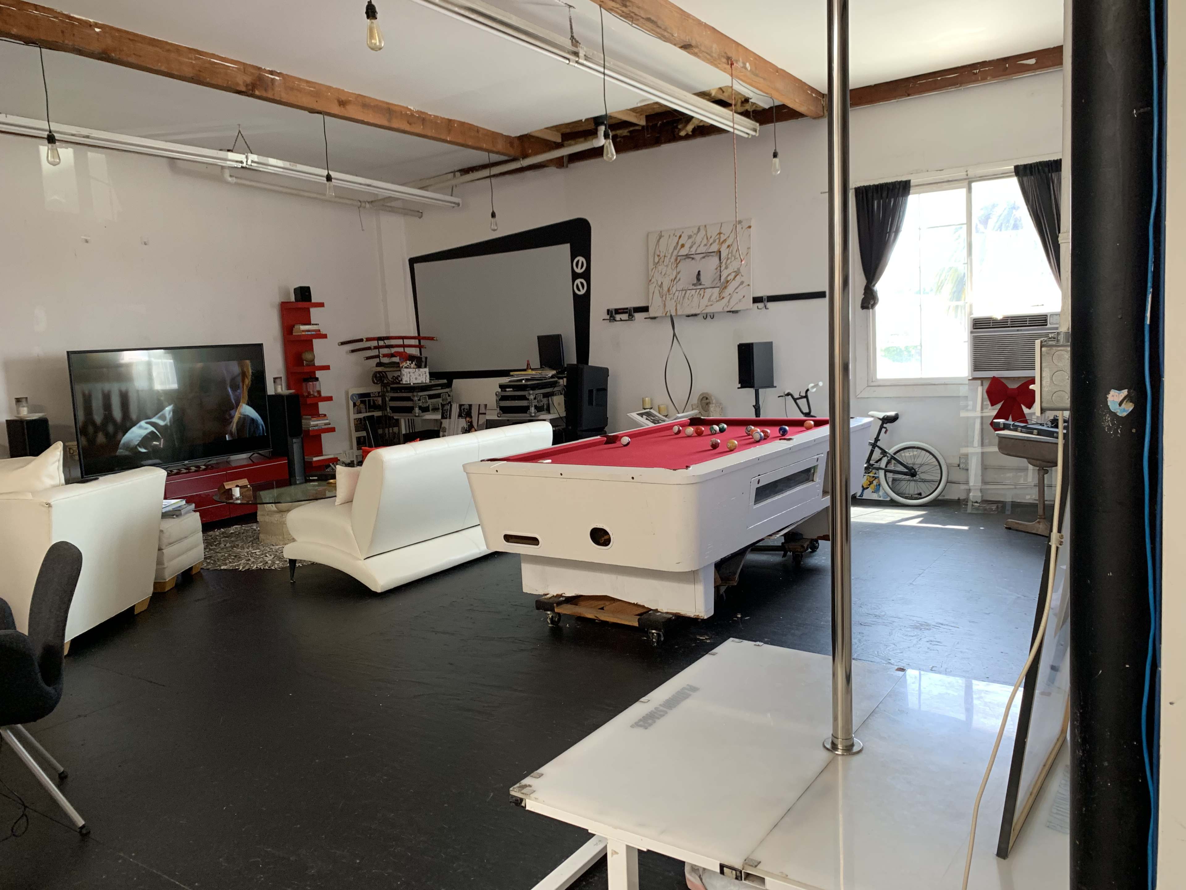 The image shows a spacious room with a pool table in the center, a large television on one side, and a bicycle leaned against the wall.