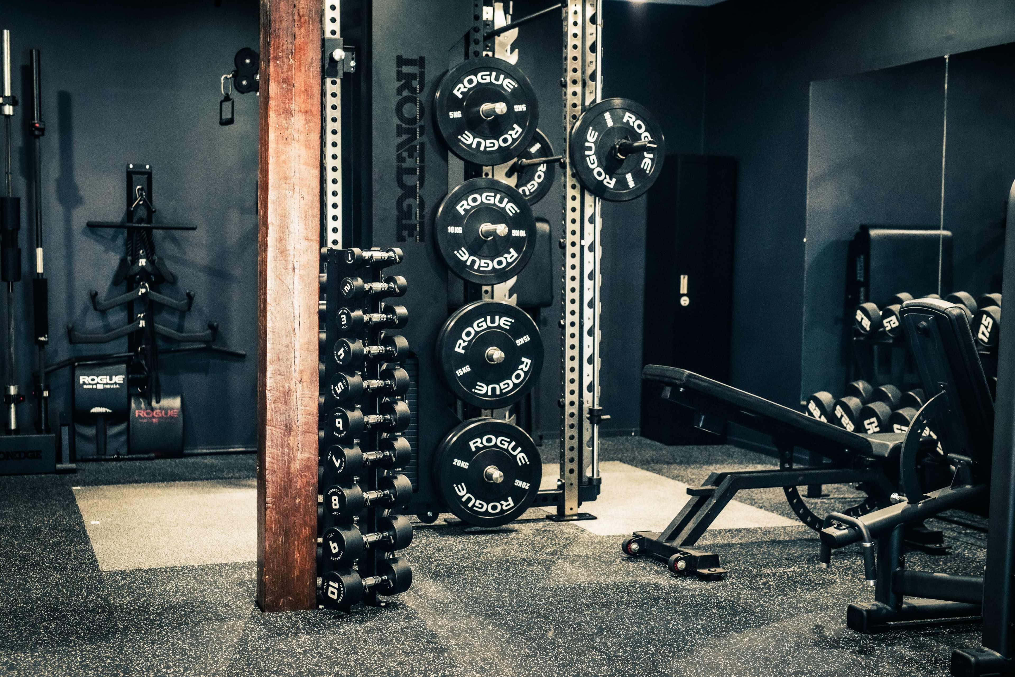 The image shows a well-equipped gym interior featuring a set of weights on a rack and various exercise equipment.