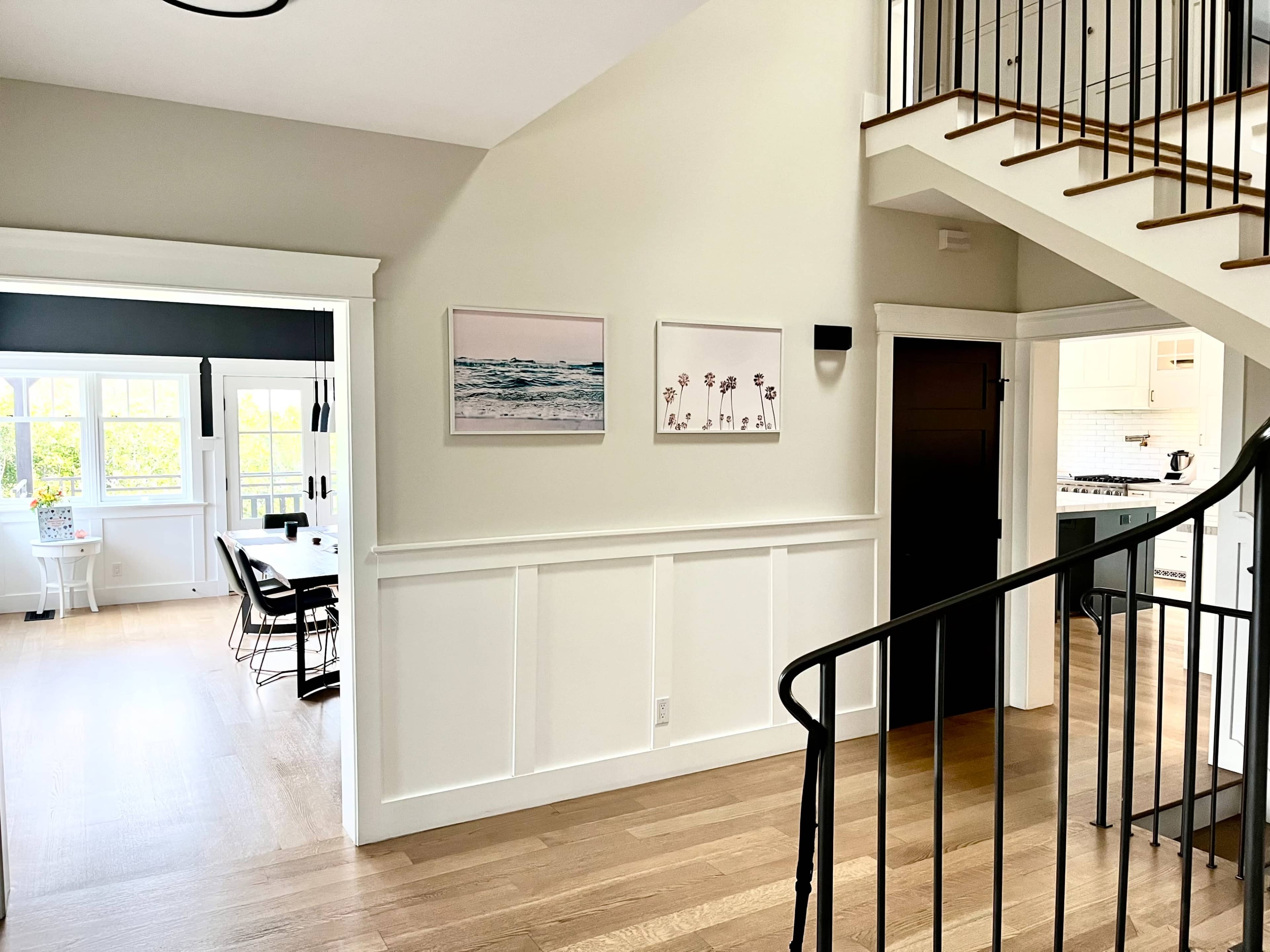 The image shows a well-lit entrance area with a staircase, featuring framed artwork on the wall and an adjacent room visible in the background.