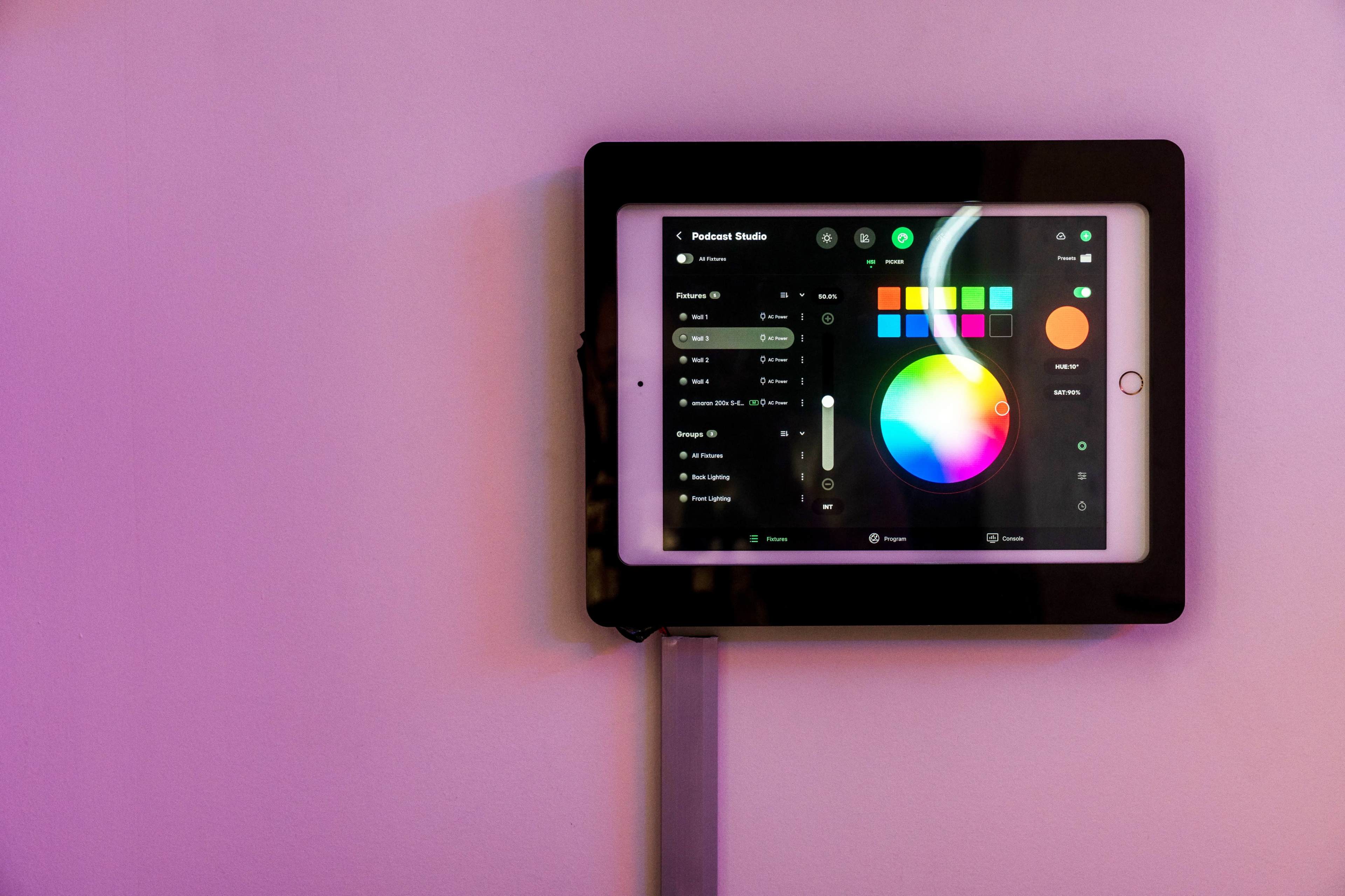A tablet mounted on a wall displays a color selection interface with a circular color wheel and various adjustment options.