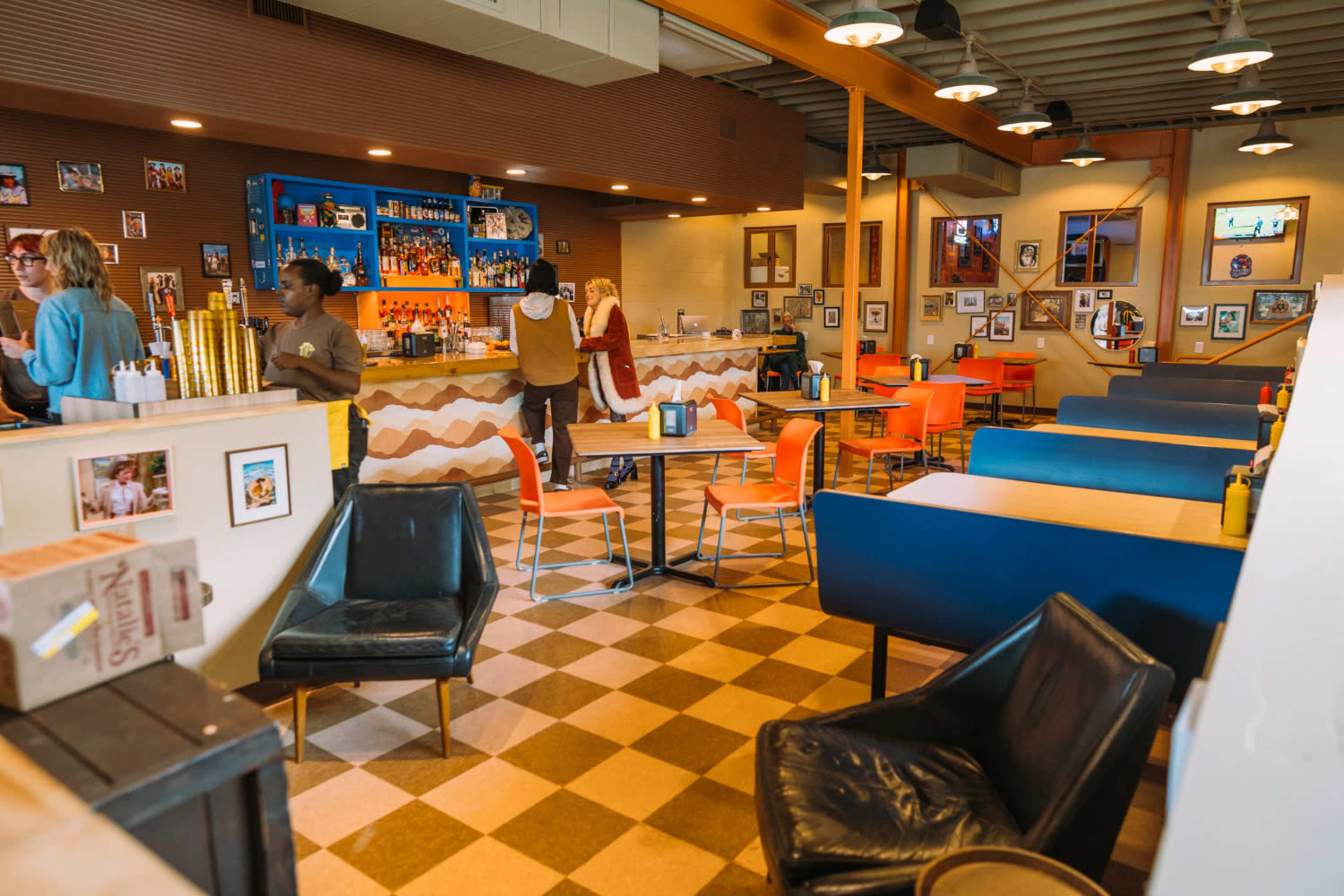 The image depicts a lively restaurant interior with a bar area, colorful seating, and framed photographs on the walls.