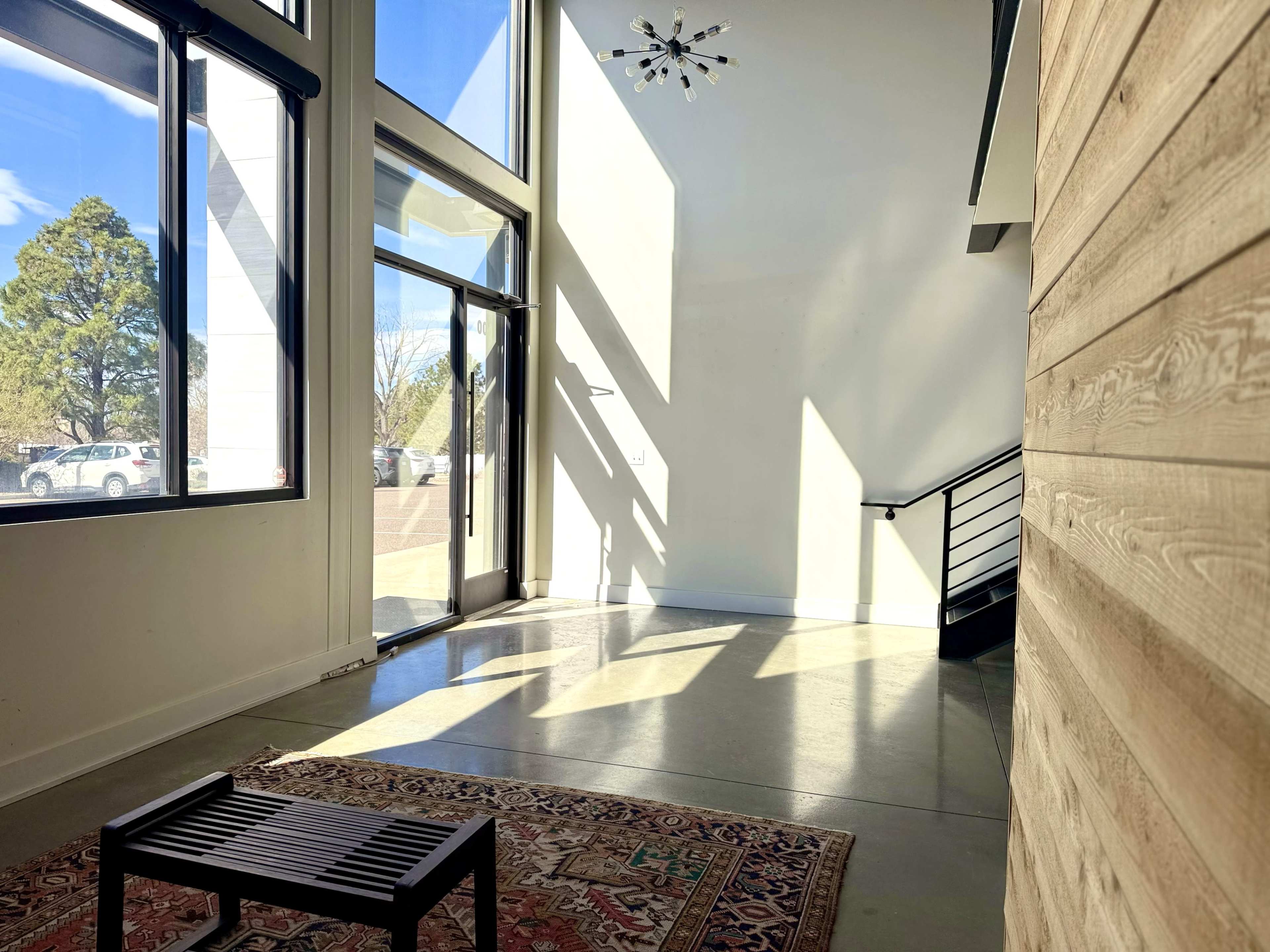 The image shows a sunlit entryway with a glass door, a staircase, and a decorative rug on the floor.
