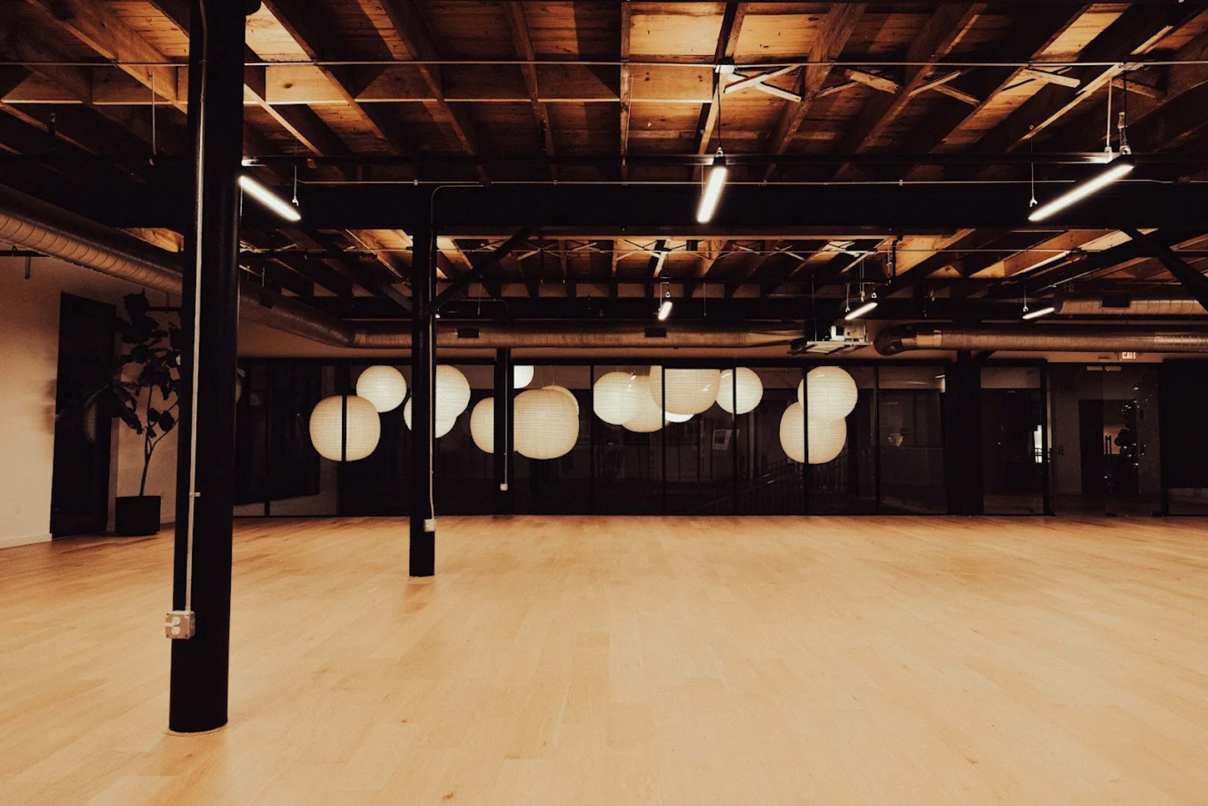 The image shows a spacious room with wooden flooring and multiple round paper lanterns hanging against a glass wall.
