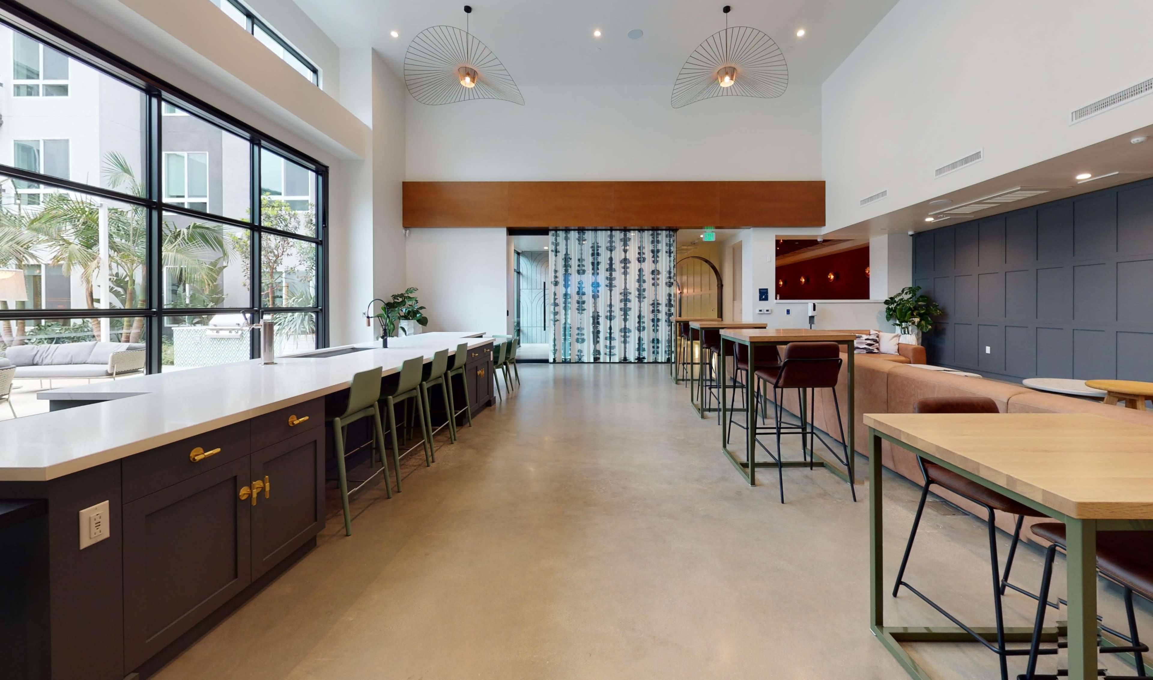 A modern indoor space featuring a long counter with bar stools on one side and tables with chairs on the other, illuminated by pendant lights.