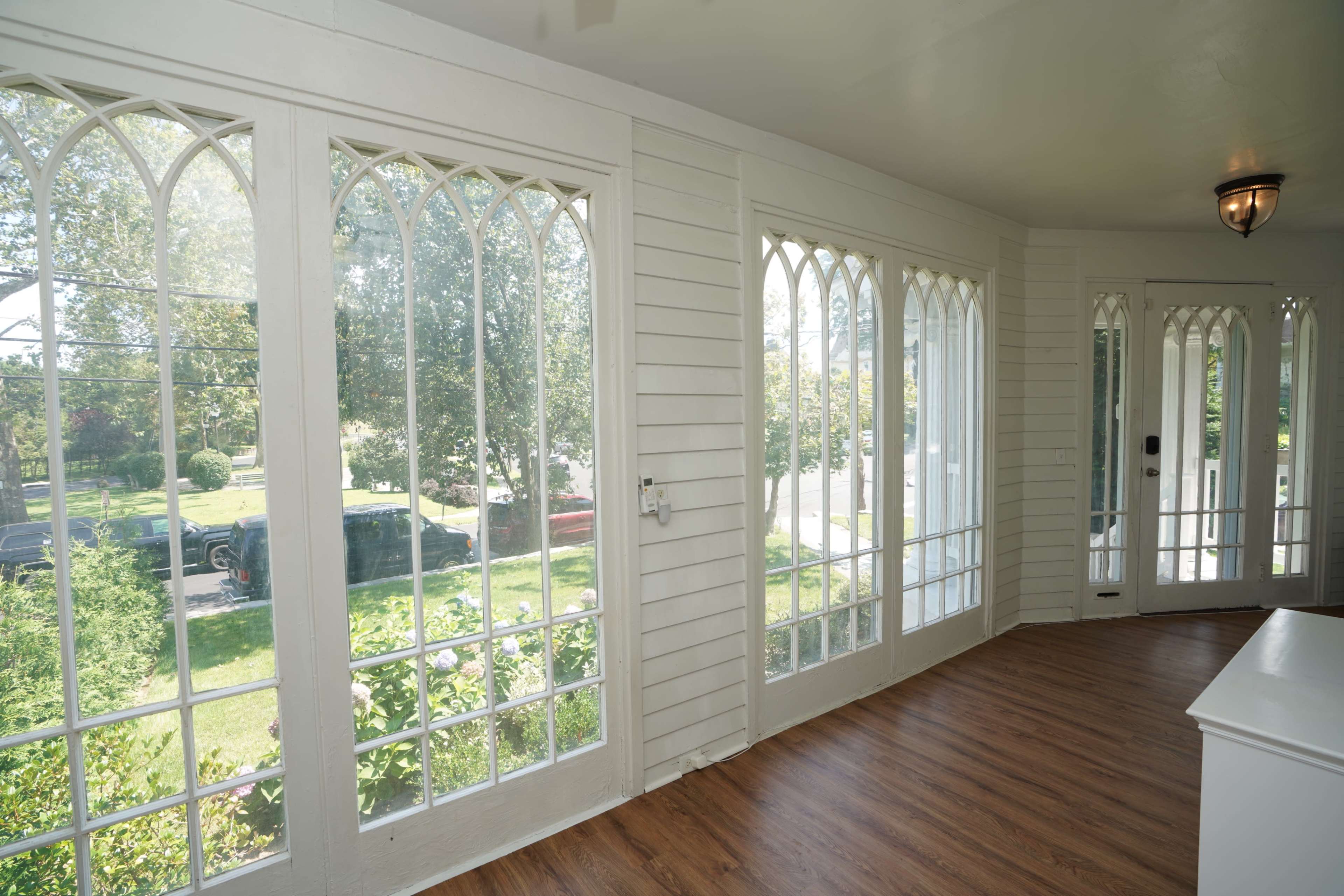 The image shows a bright, airy room with large arched windows overlooking a green yard and driveway.