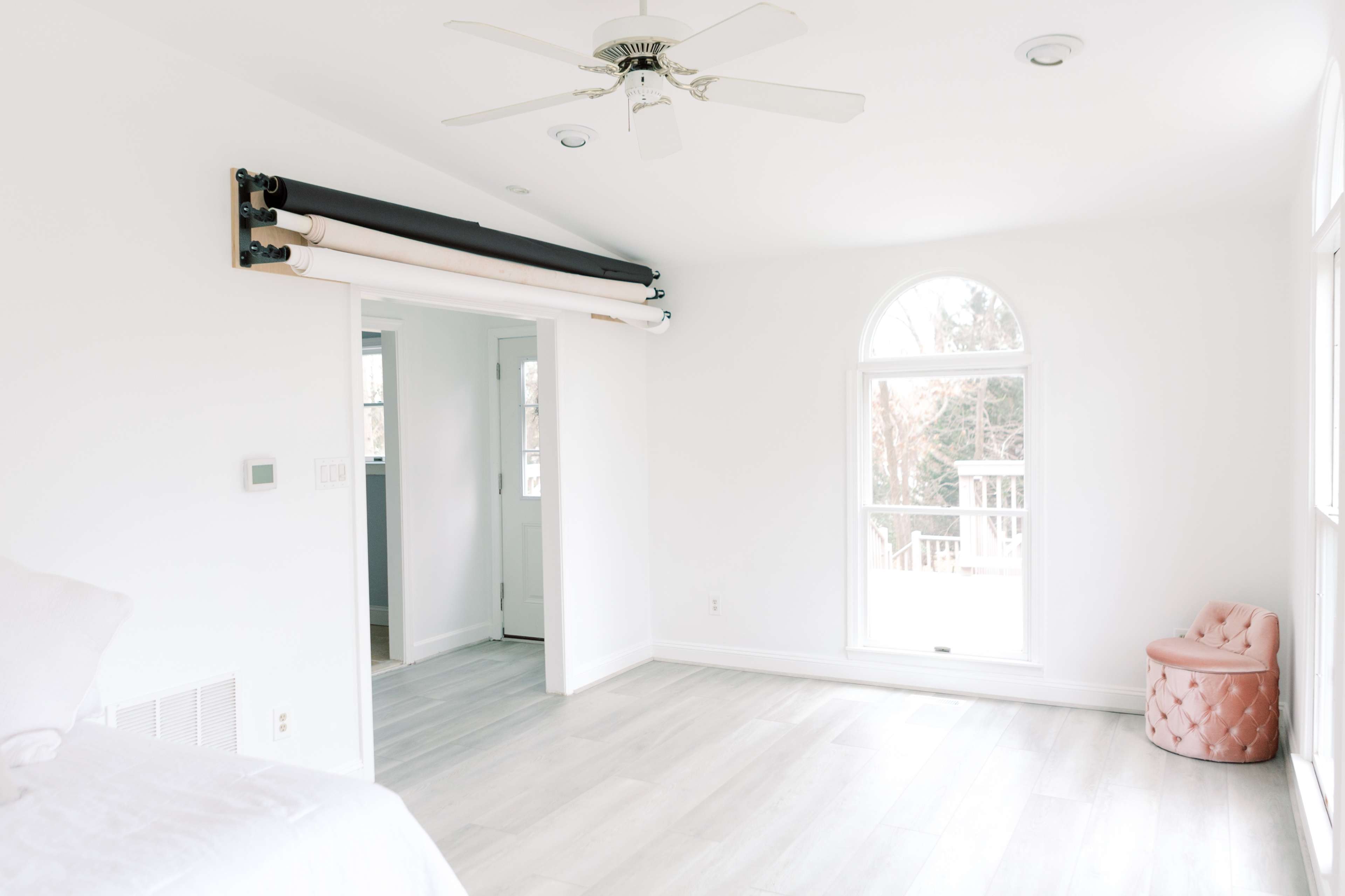 A bright, minimalistic room features a mounted roll of paper on the wall, a ceiling fan, and large windows letting in natural light.