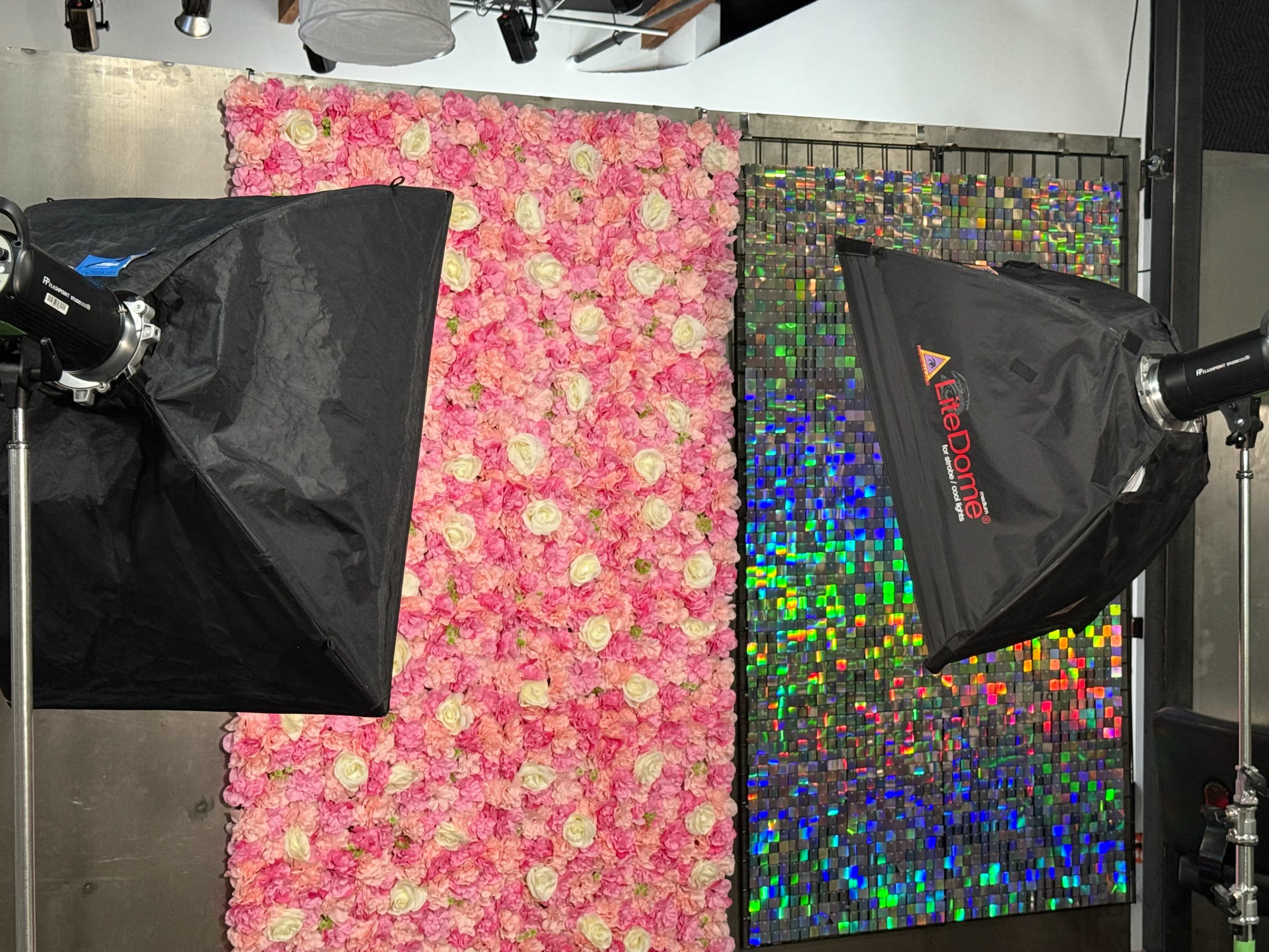 The image shows a photography setup featuring a pink flower wall on the left and a colorful mosaic wall on the right, illuminated by two softboxes.