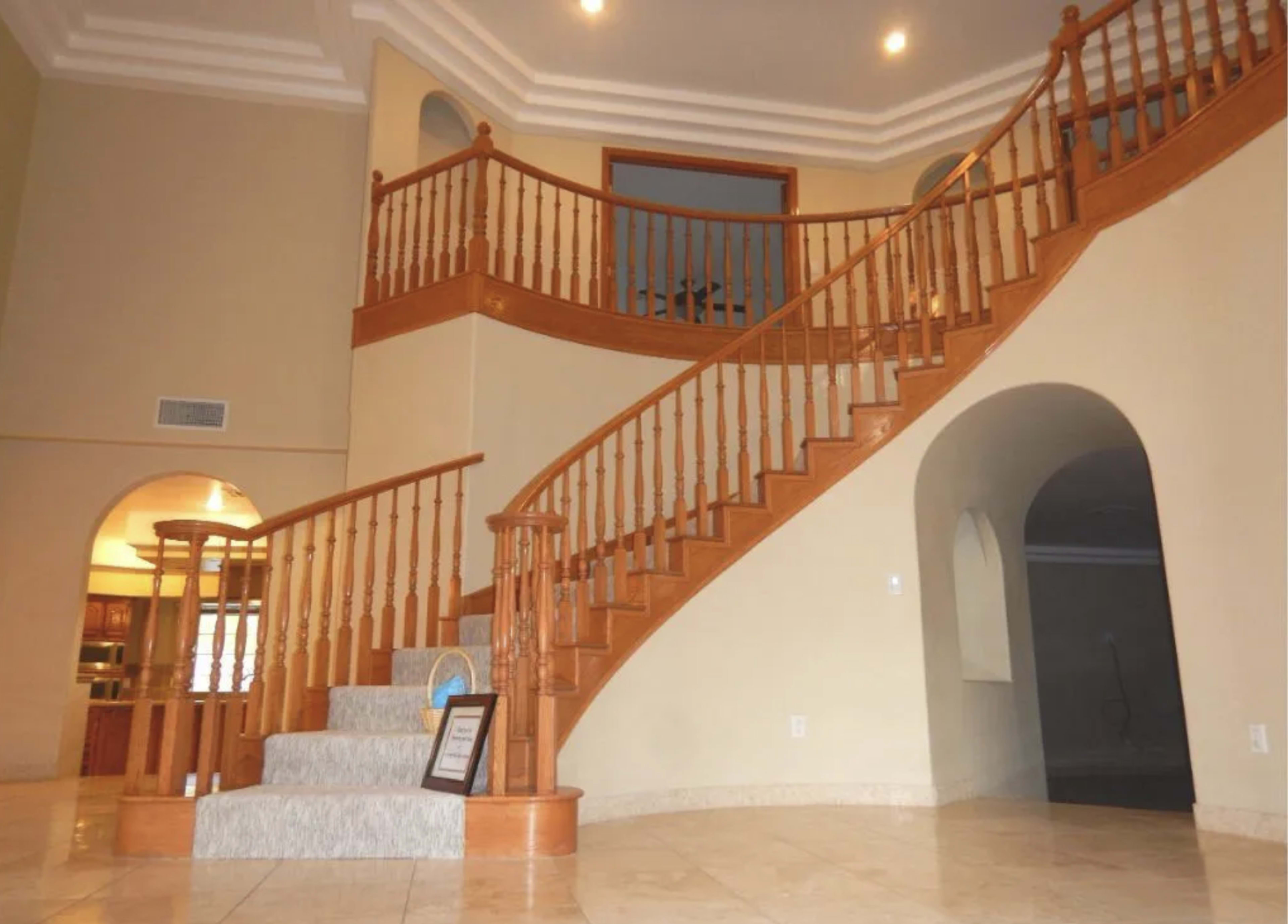 The image shows a spacious foyer with a wooden staircase featuring a curved design and decorative railing, leading to an upper level.