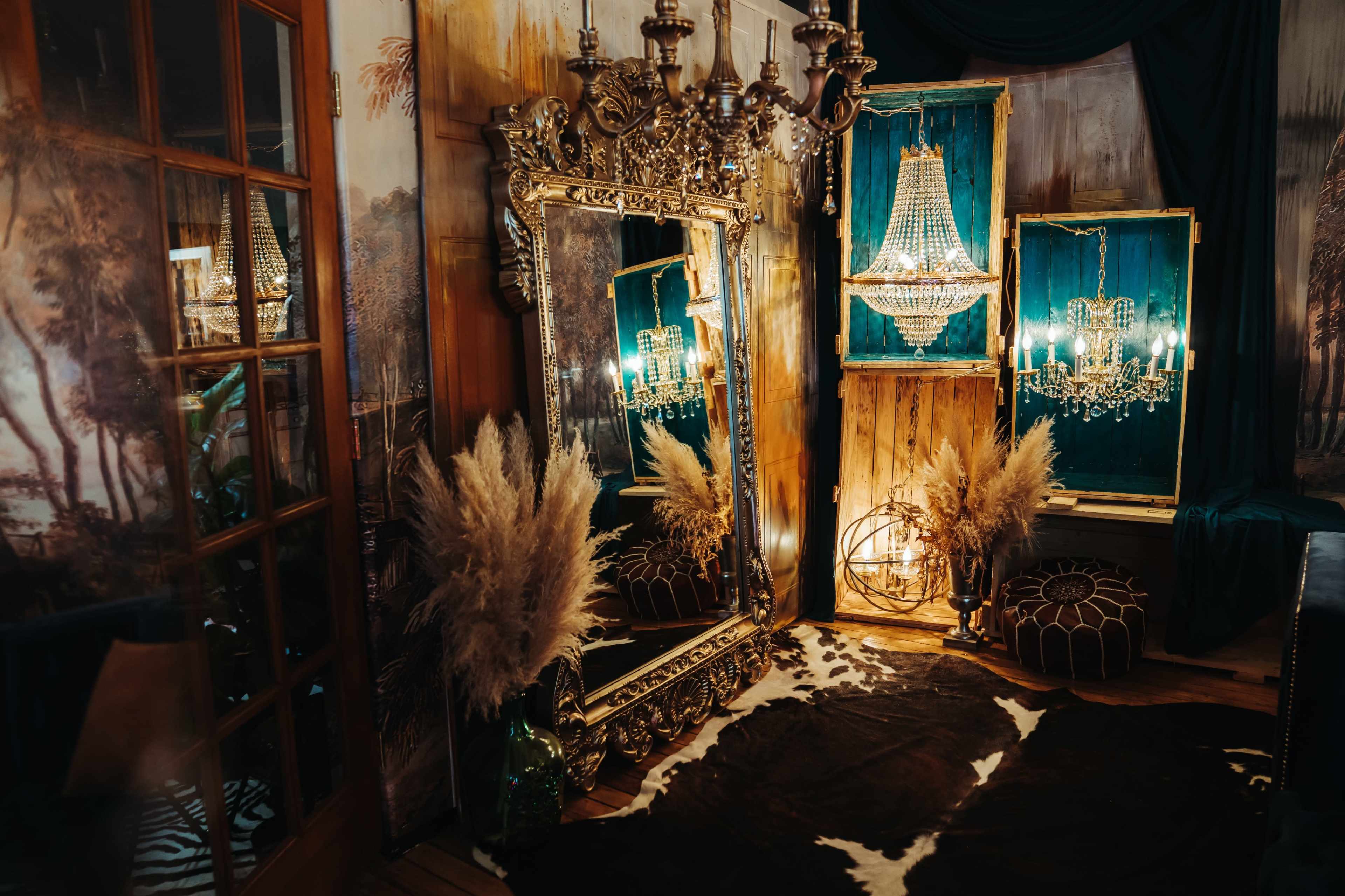 The image features an elegantly decorated interior with a large ornate mirror, multiple chandeliers, and a cowhide rug, surrounded by rich textiles and decorative elements.
