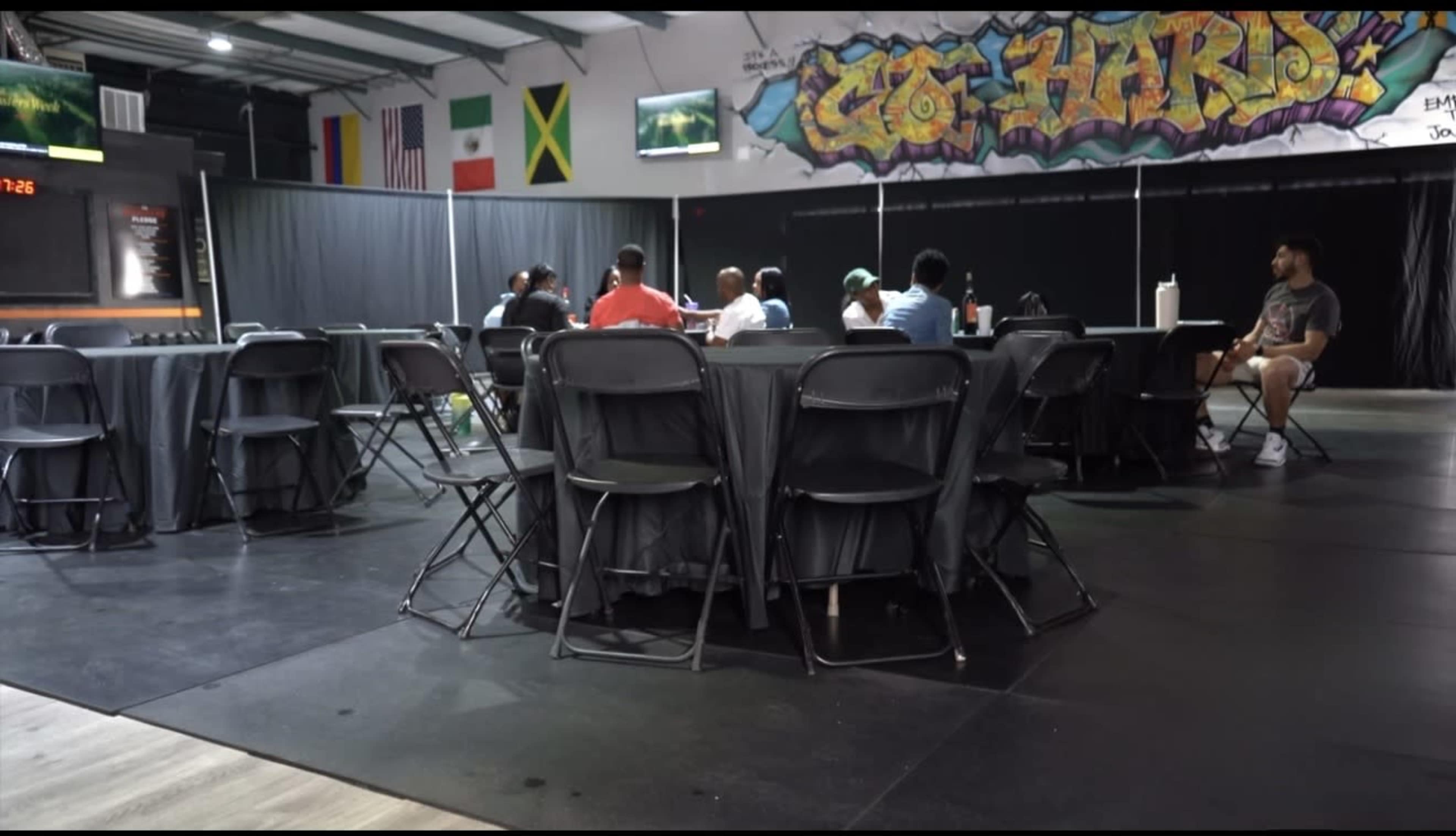 A group of people is seated around several tables in a large, open room with colorful graffiti on the walls.