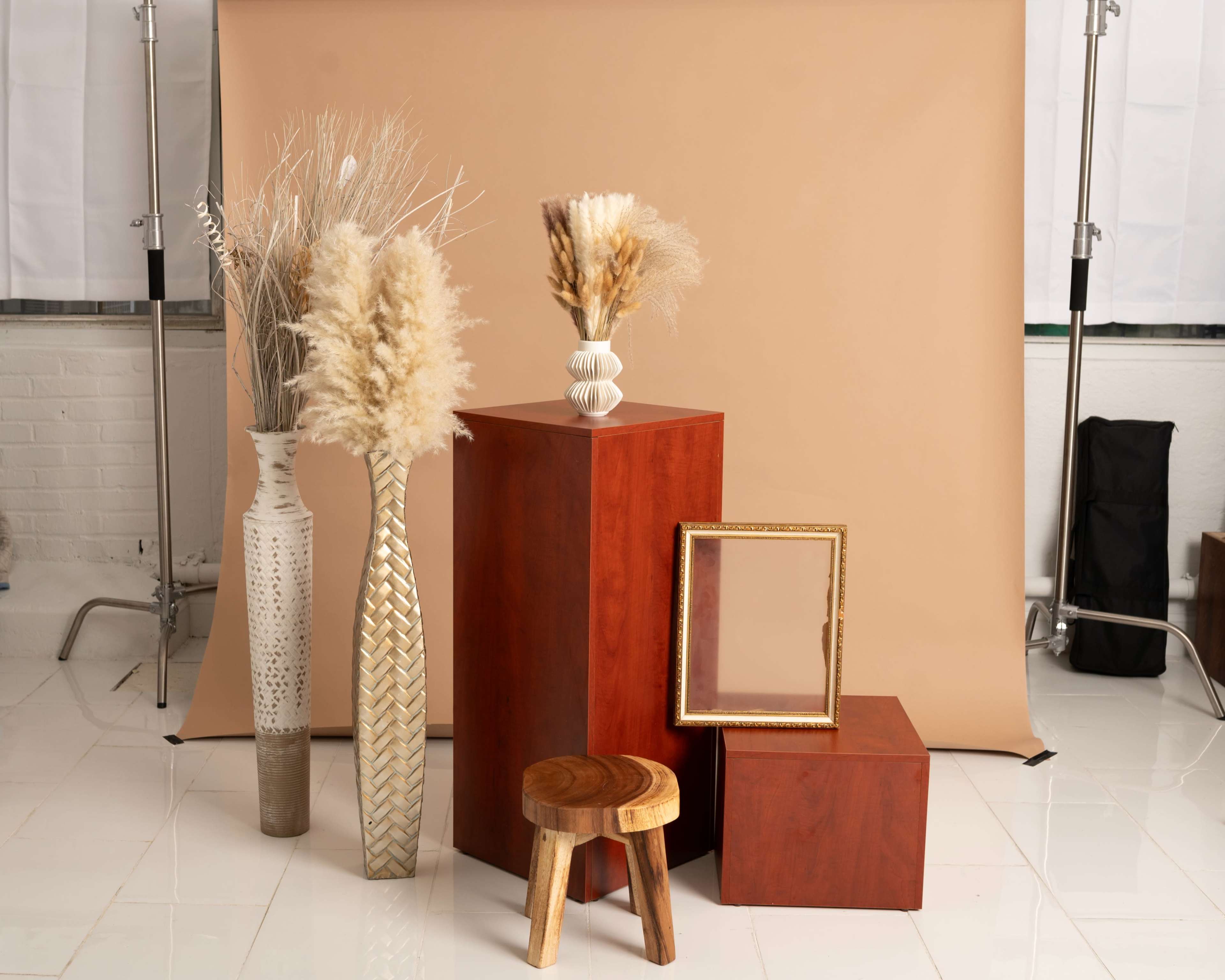 The image features a styled arrangement of decorative vases and wood furniture against a beige backdrop in a studio setting.