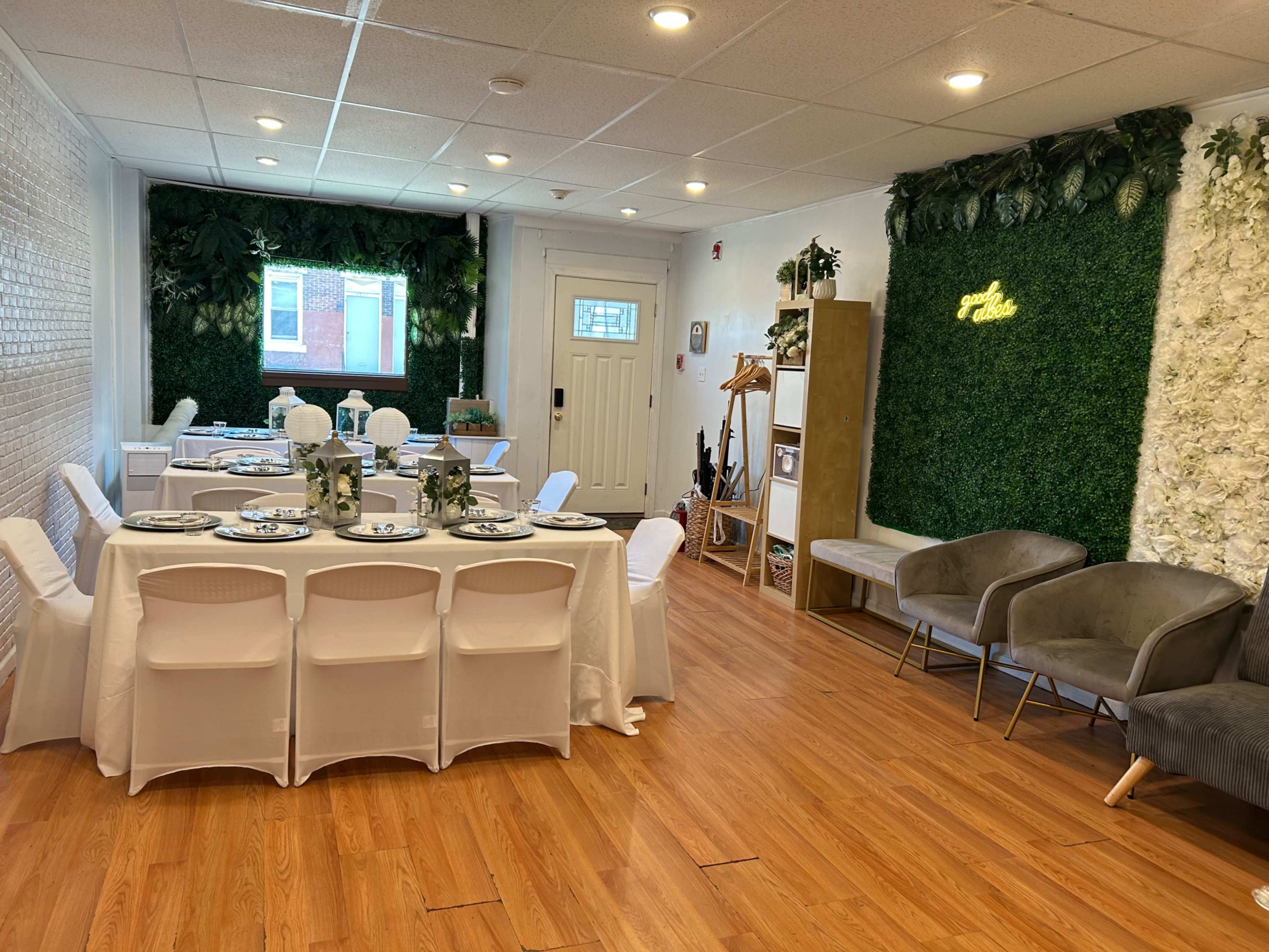 The image shows a brightly lit dining area with a long table set for a meal, surrounded by greenery and decorative plants on the walls.
