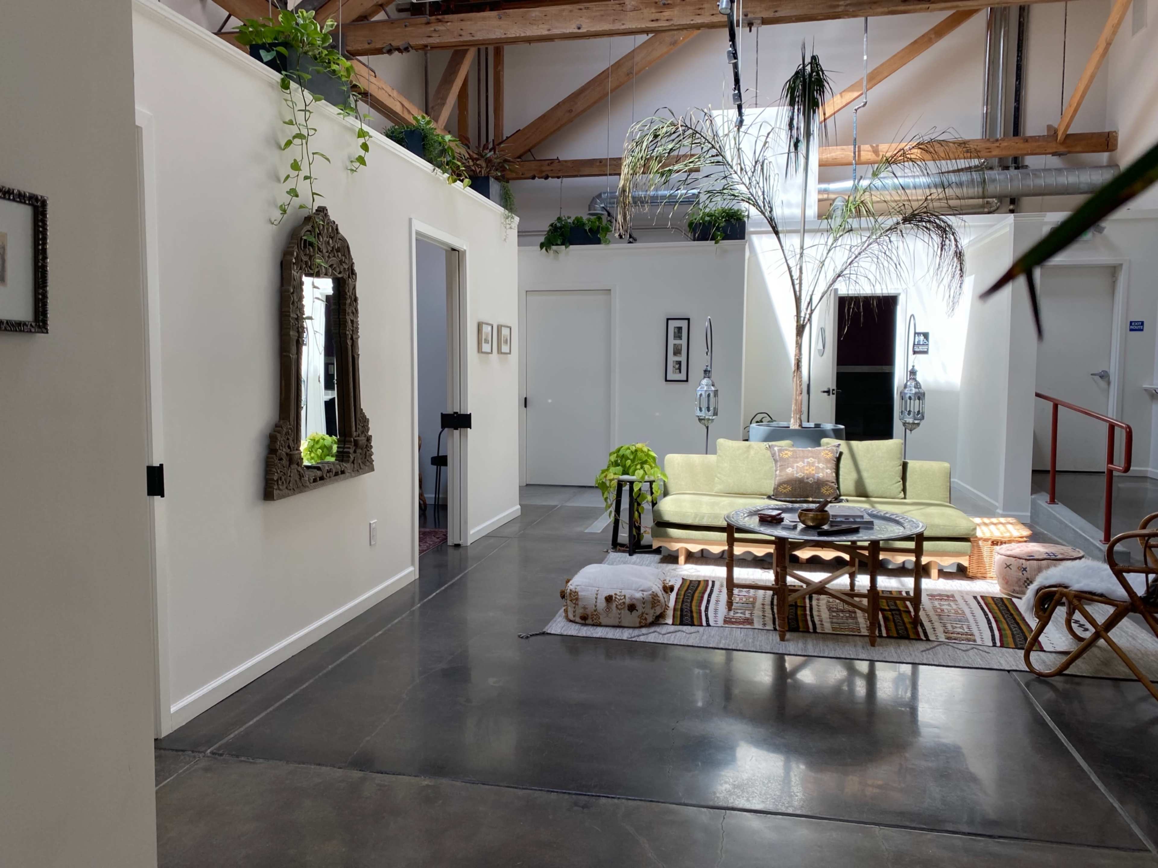 A bright, open living space with a green couch, a coffee table on a patterned rug, and decorative plants hanging from the ceiling.