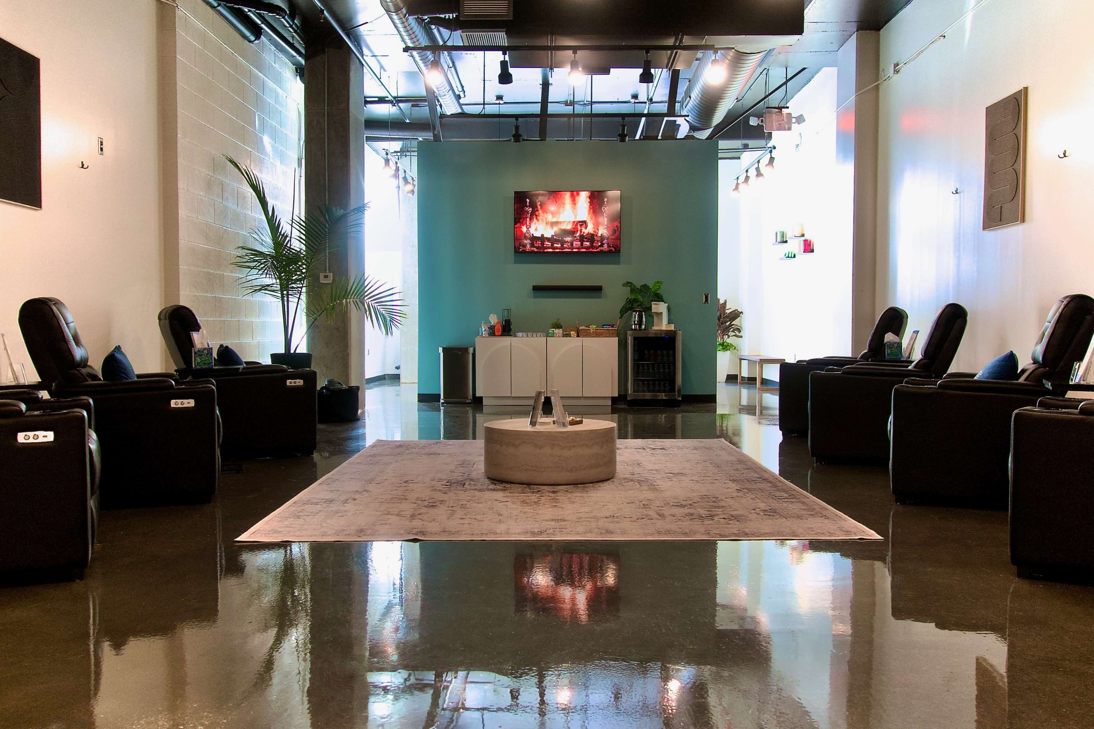 The image shows a modern relaxation lounge with plush seating arranged around a central area, featuring a large screen displaying a fireplace.