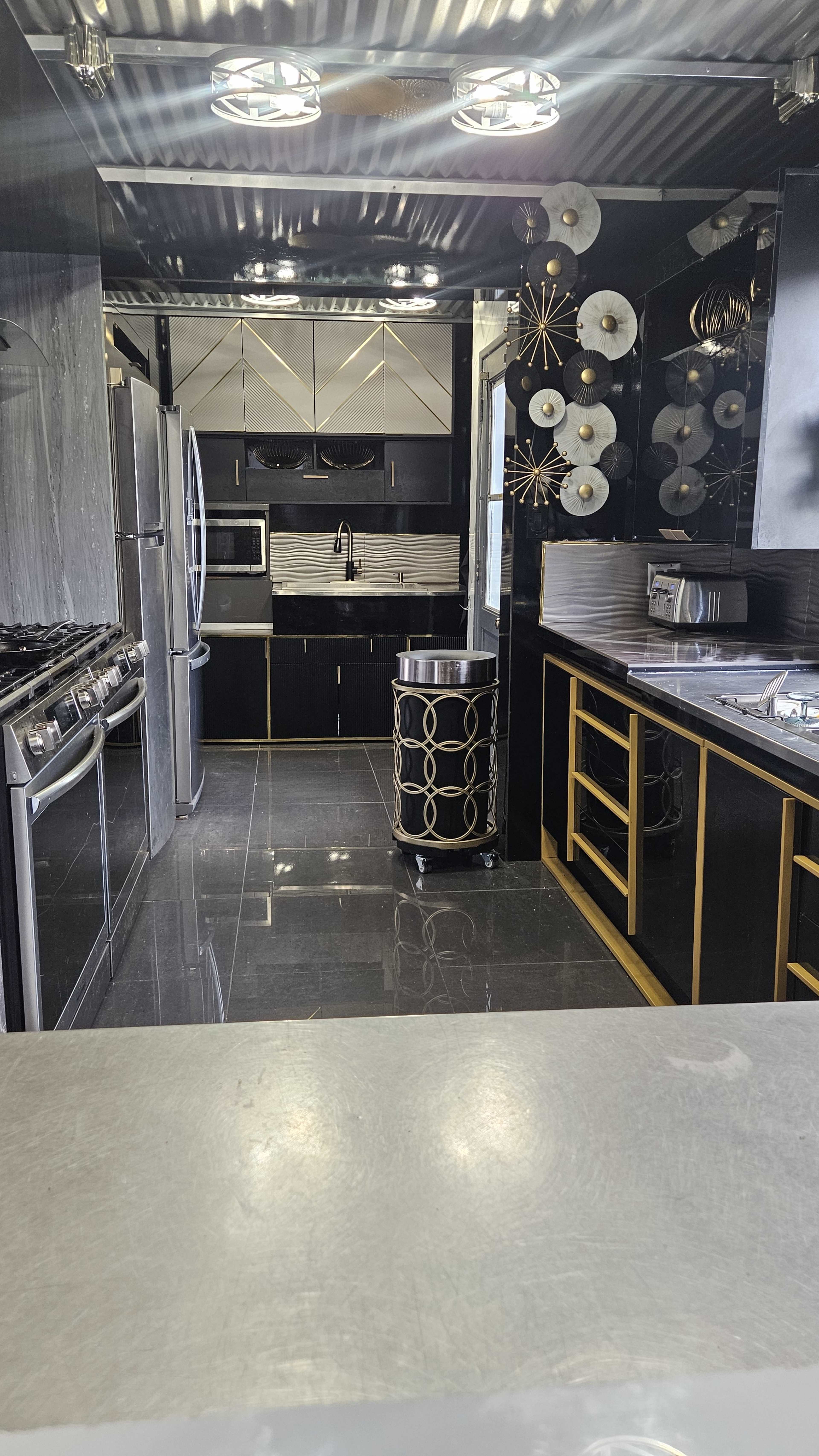 The image shows a modern kitchen with stainless steel appliances, dark cabinetry, and decorative wall features.