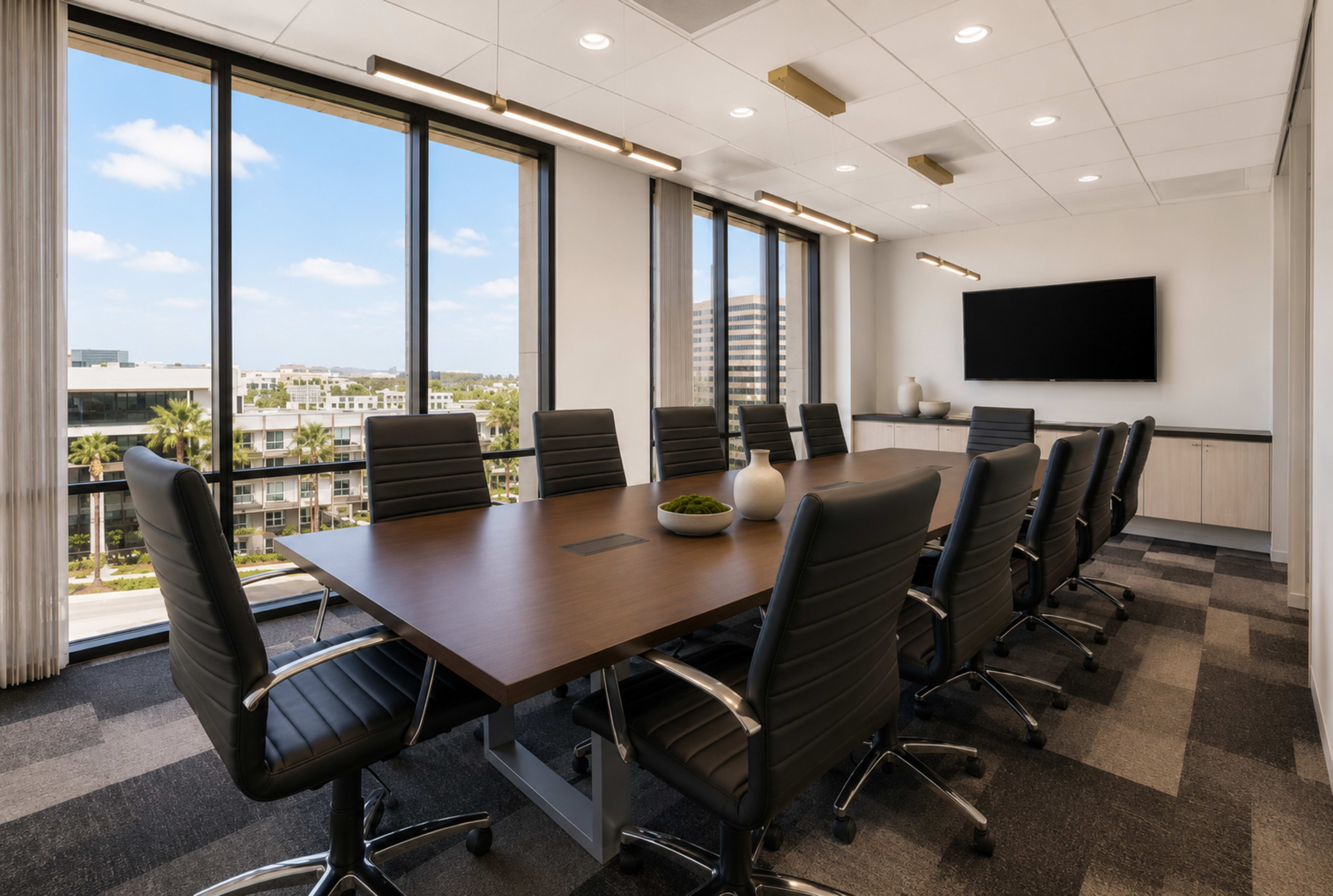 The image shows a modern conference room with a large wooden table surrounded by black leather rolling chairs, featuring large windows that allow natural light and views of an outdoor landscape.