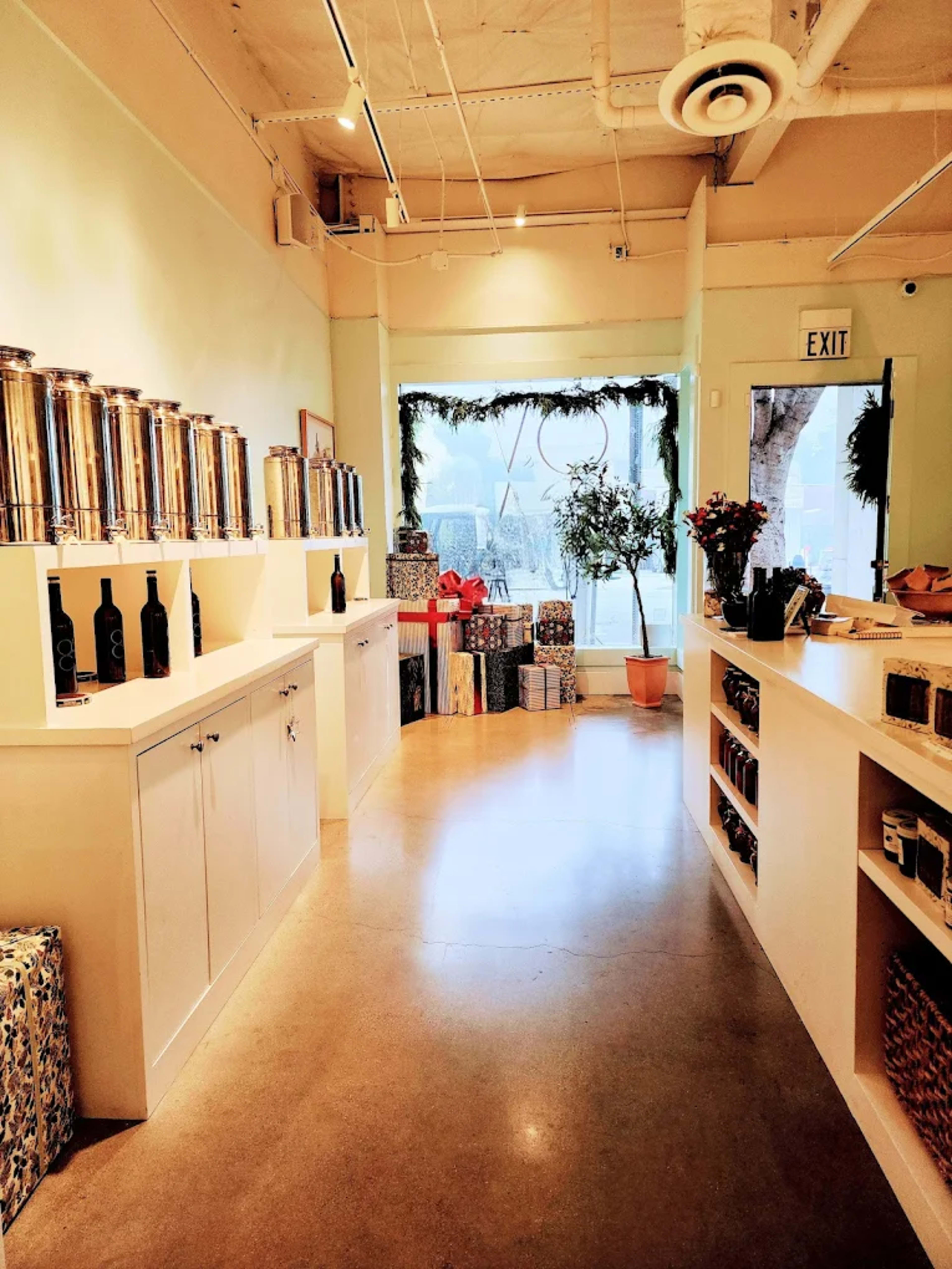 The image shows a bright retail space featuring stainless steel containers, wine bottles on display, and wrapped gifts arranged near a large window.