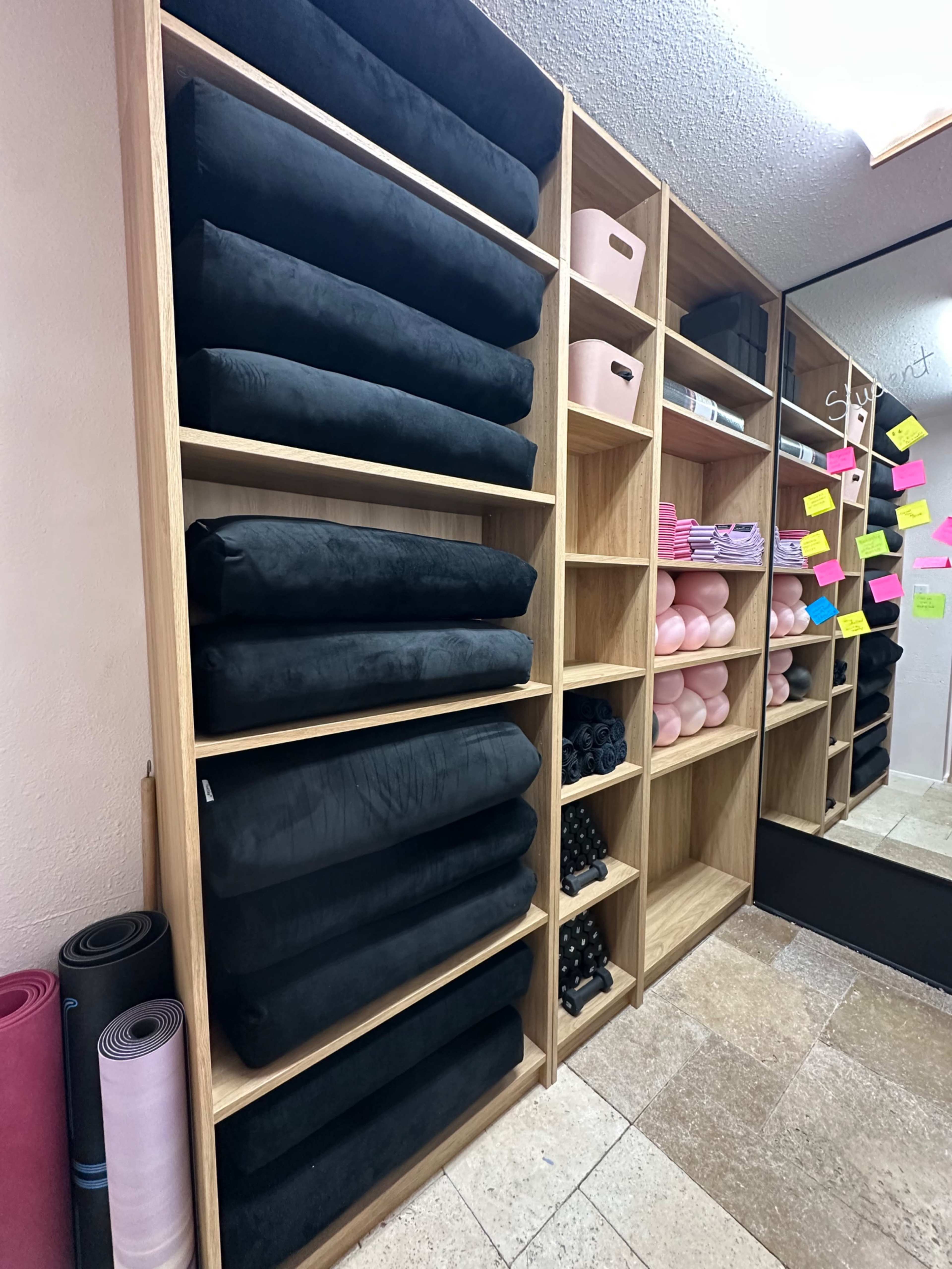The image shows a neatly organized storage area with shelves displaying rolls of black fabric and various supplies, including pink storage boxes and yoga mats.