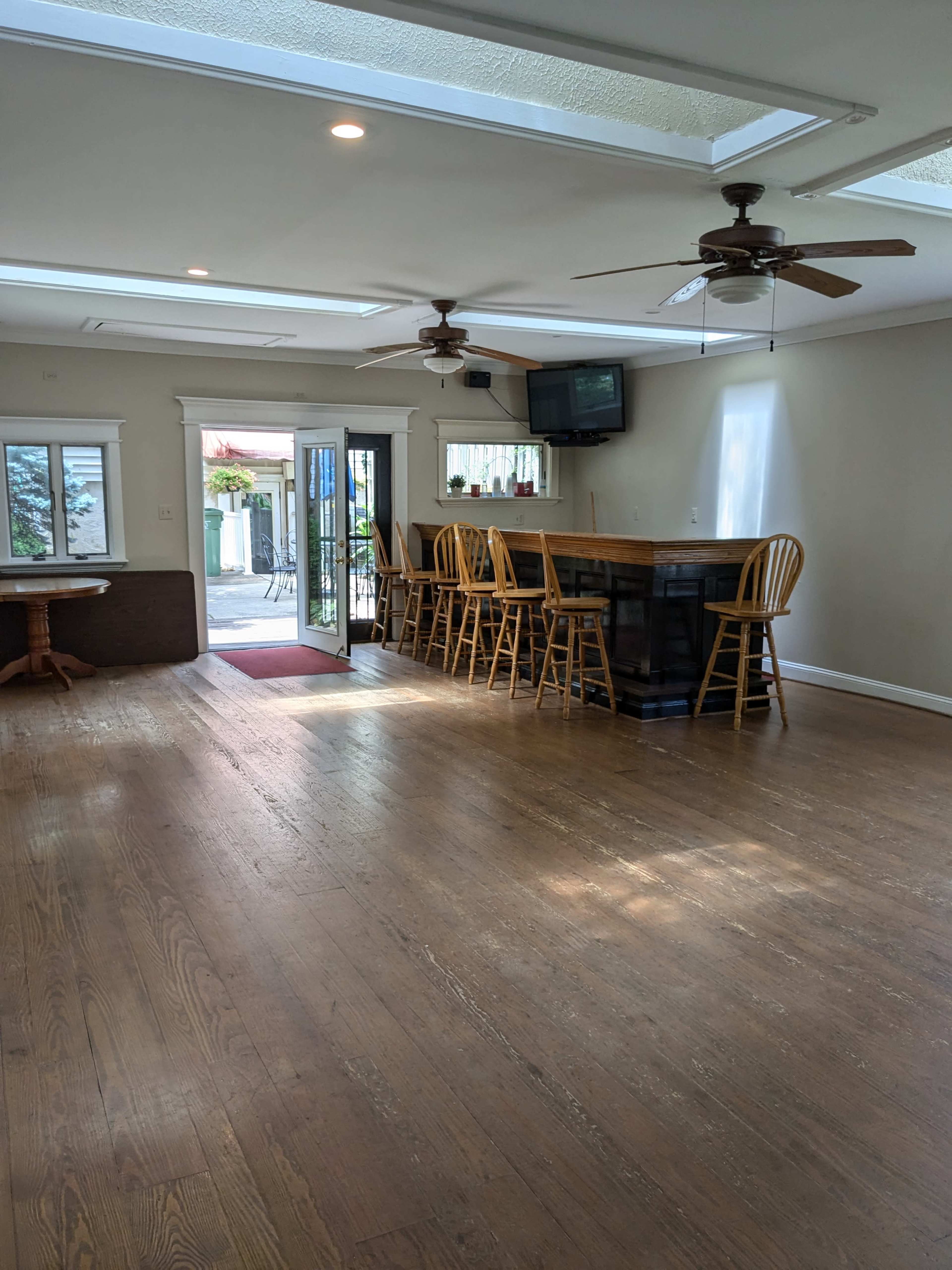 A spacious, well-lit indoor area featuring a bar counter with seating, two ceiling fans, and a door leading to an outdoor space.
