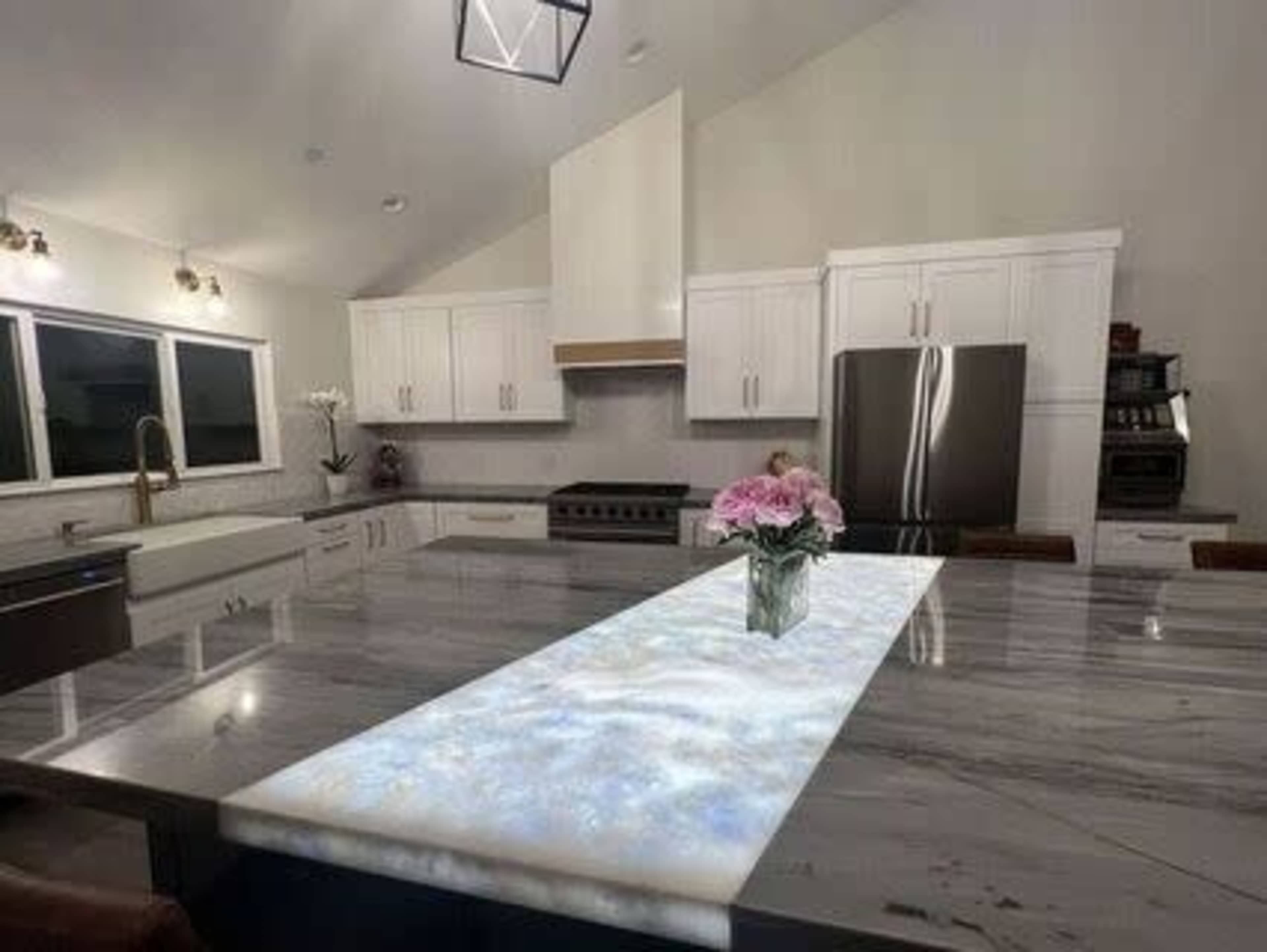 A modern kitchen features a large marble island with a glowing centerpiece and white cabinetry.