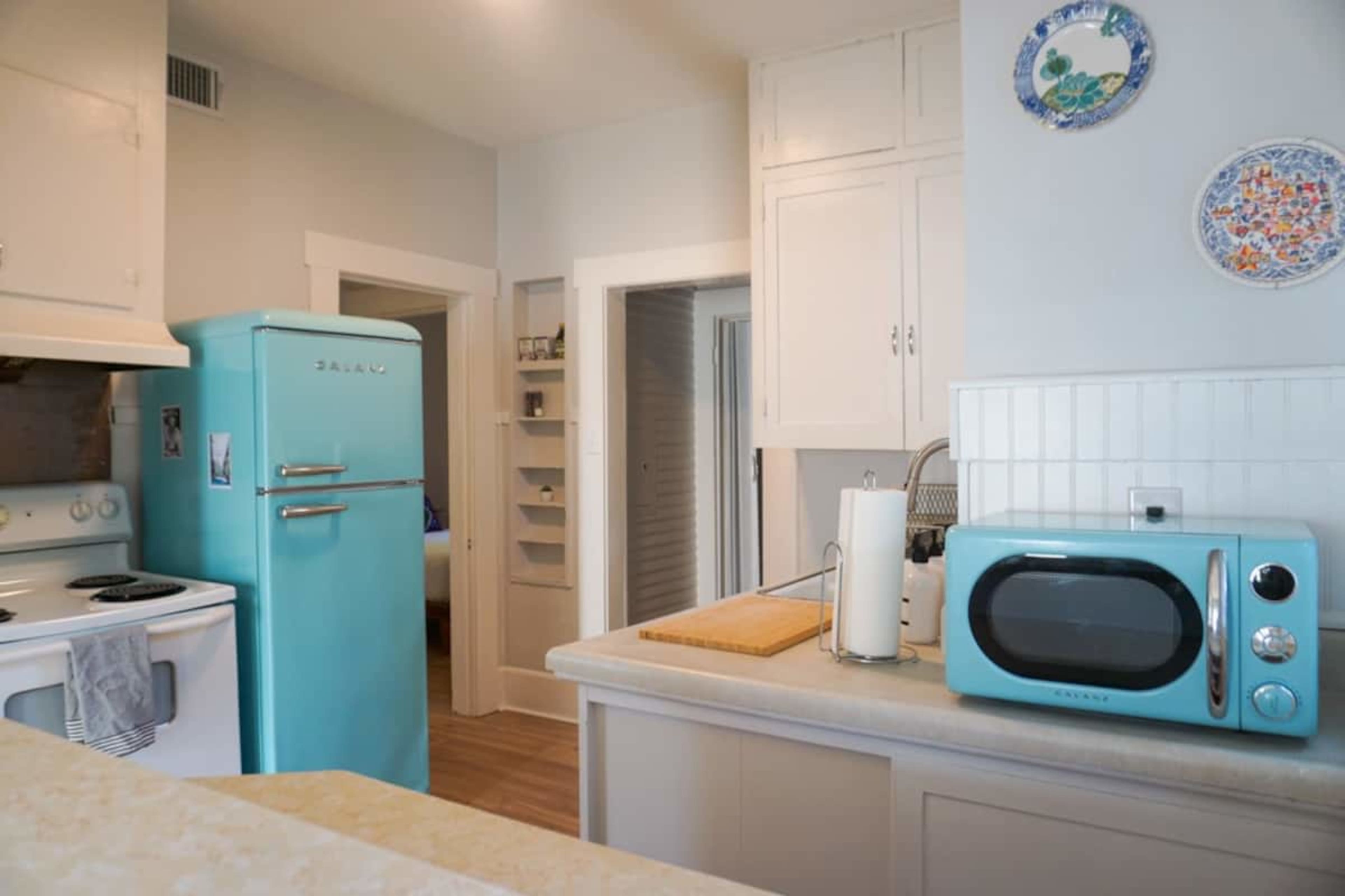 A retro-styled kitchen featuring a turquoise refrigerator and microwave, with white cabinetry and a countertop.
