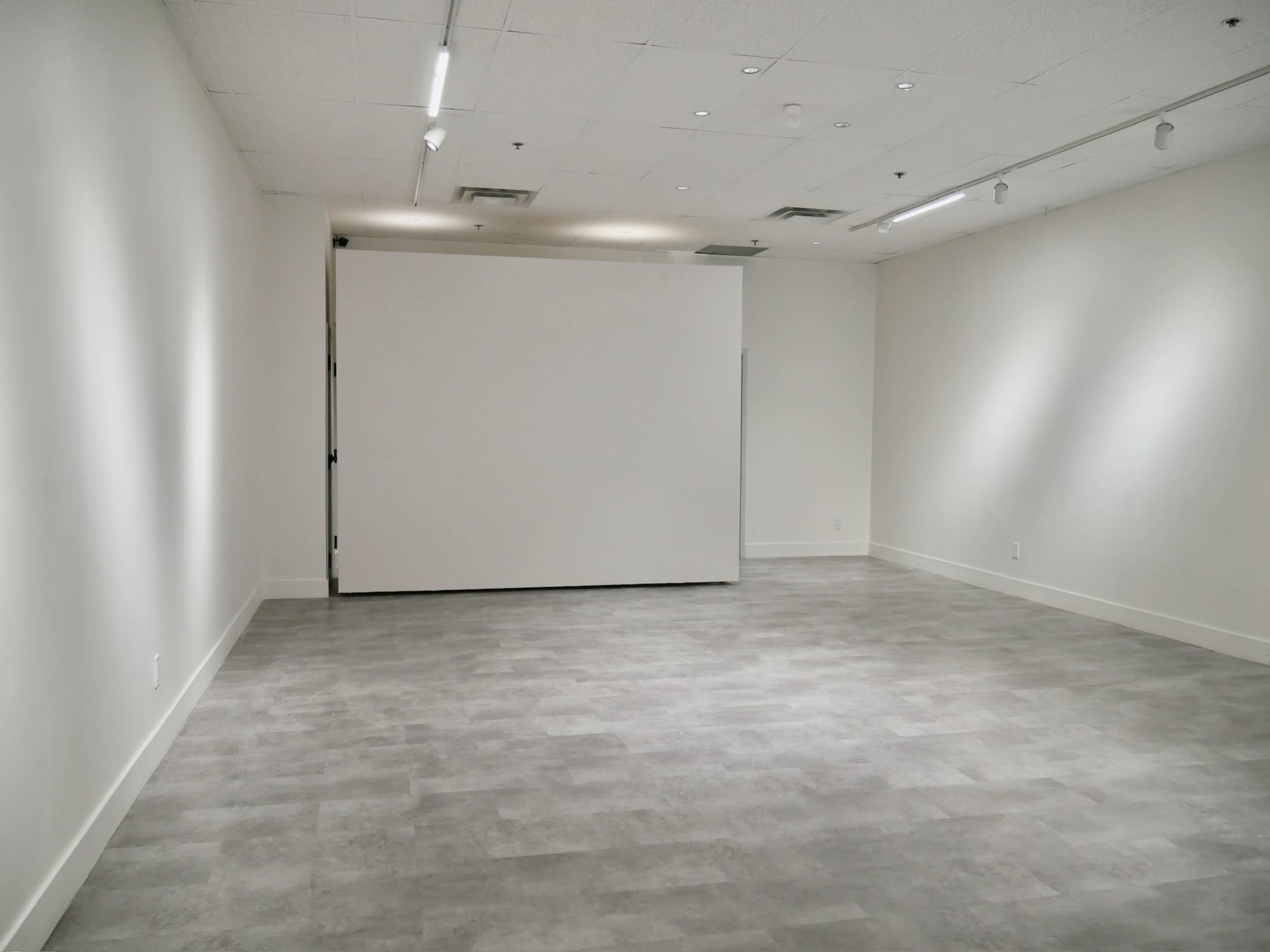 A spacious, empty room with gray flooring and white walls, featuring a large blank screen at one end.