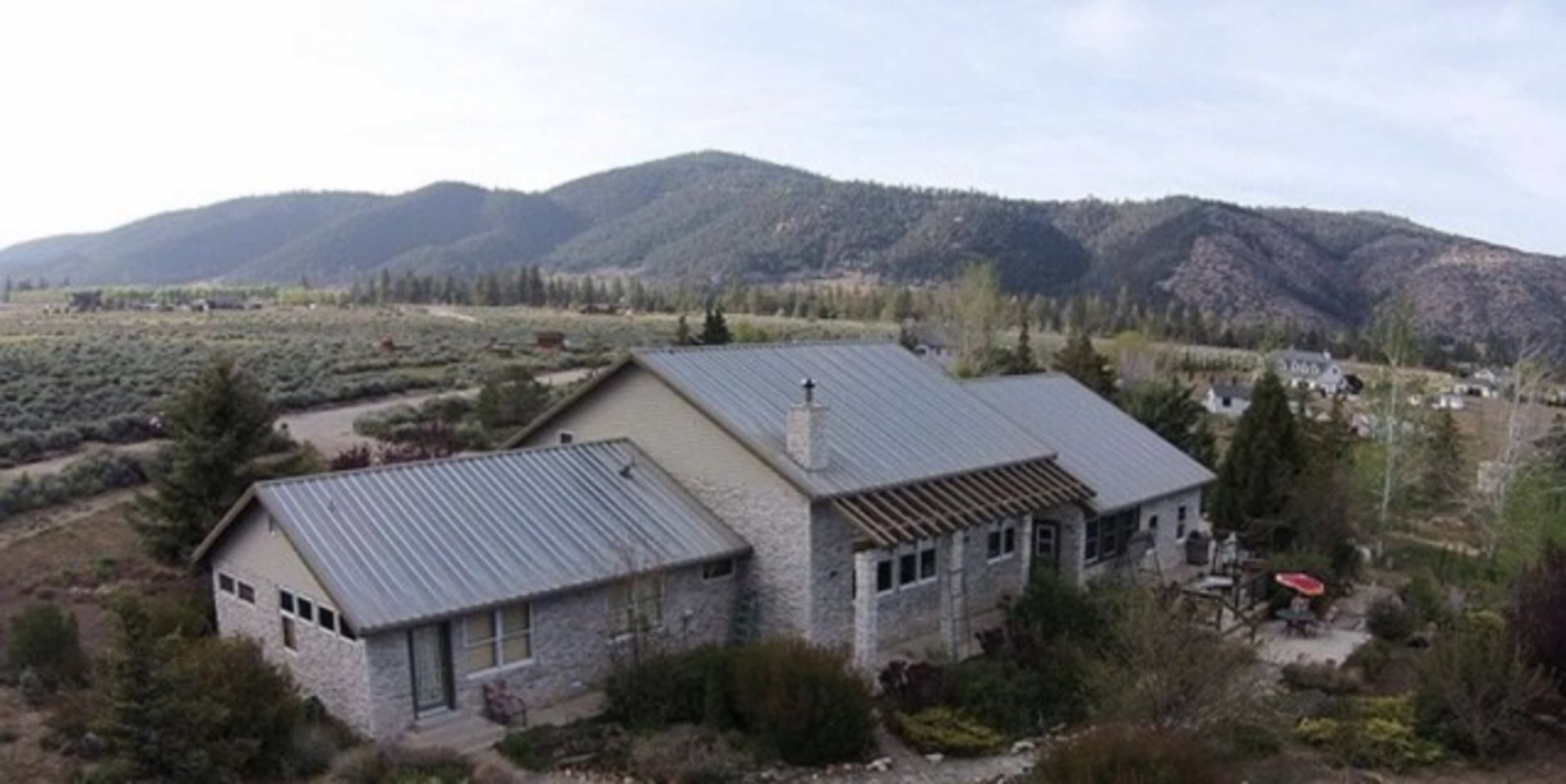 A large, single-story house with a metal roof situated near rolling hills and mountains in a rural area.