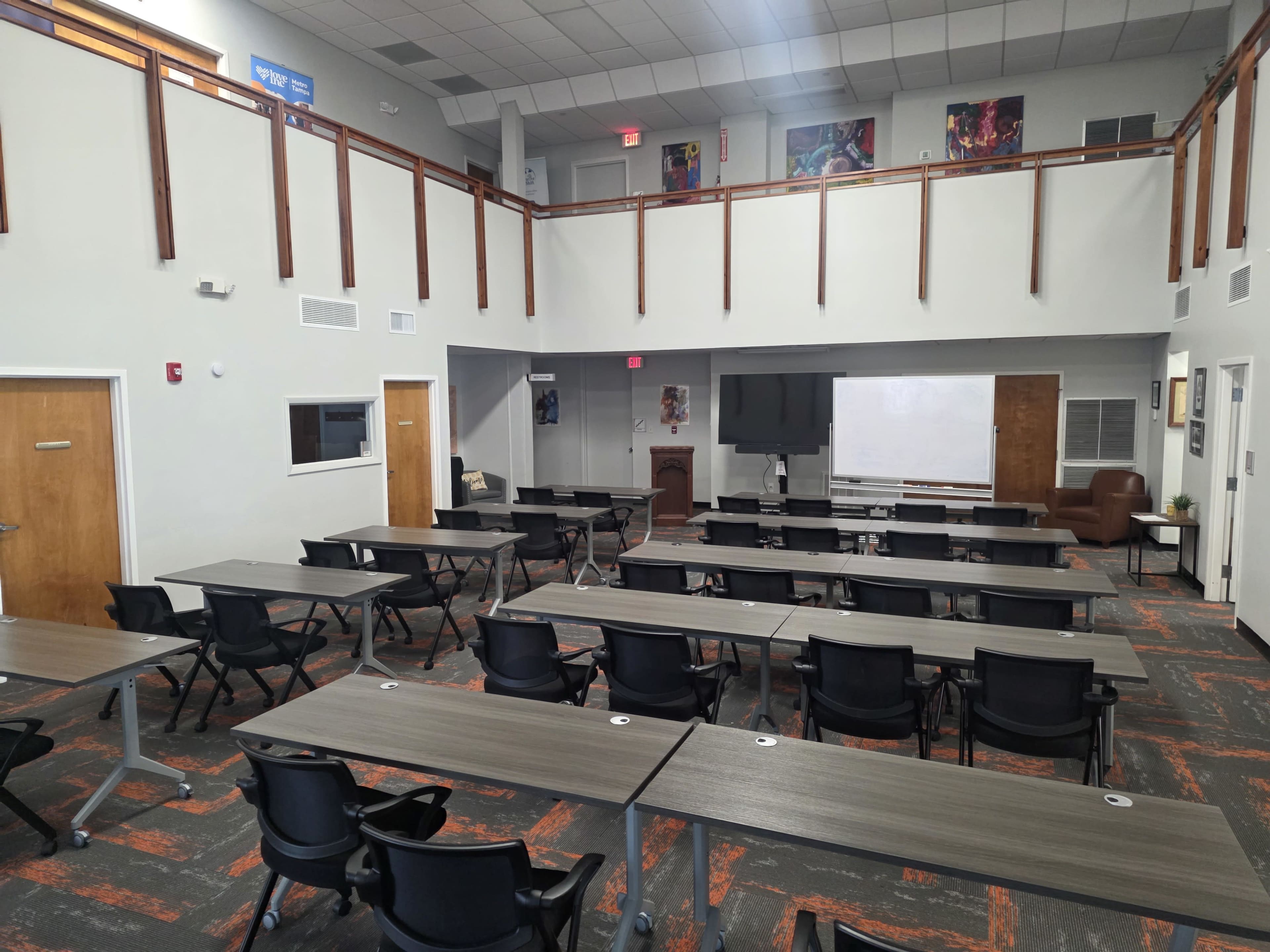 The image shows a modern classroom setup with multiple rows of tables and chairs, equipped with a large screen and a whiteboard at the front.