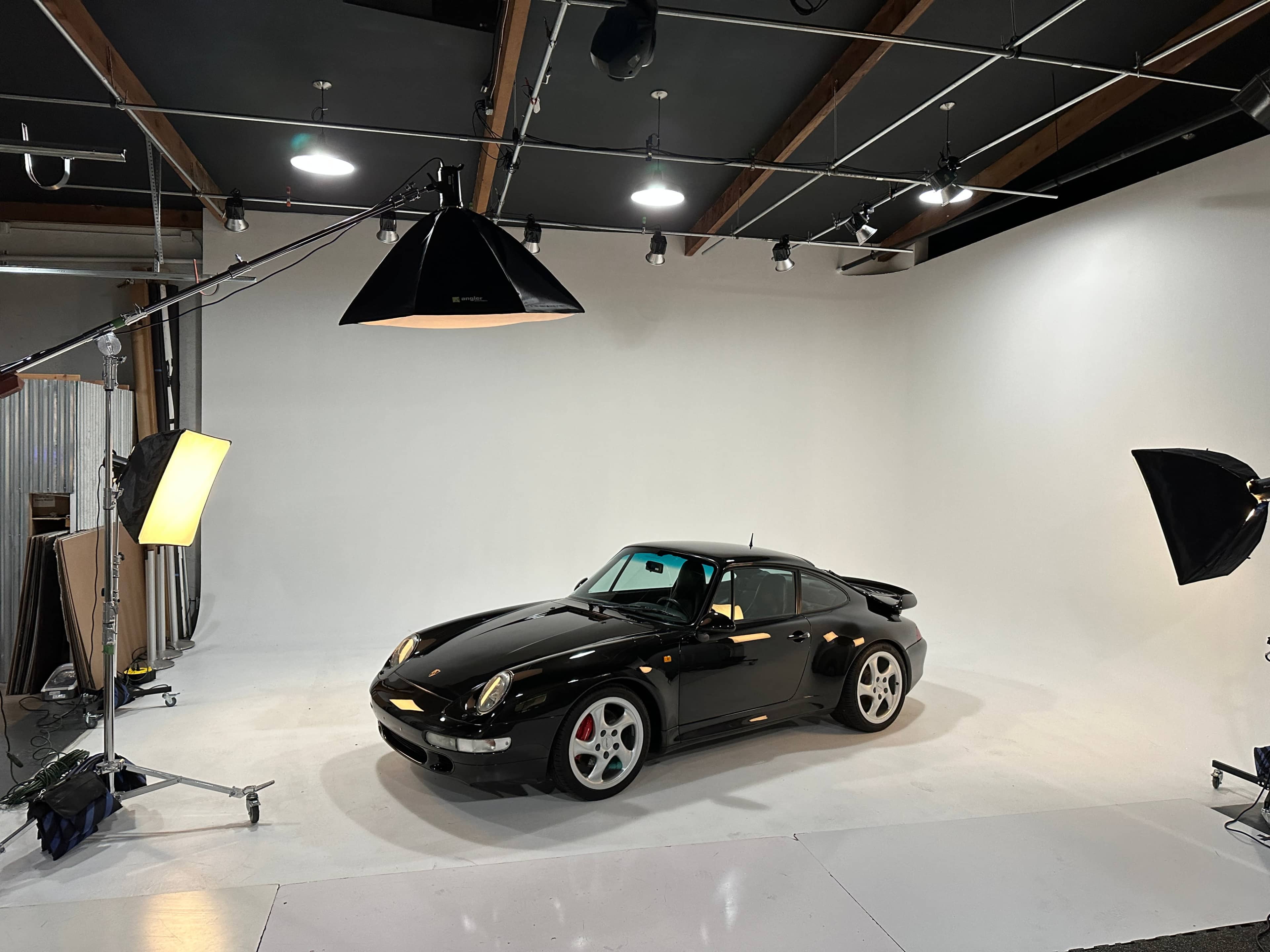 A black sports car is positioned in a studio with bright lighting and a white backdrop.
