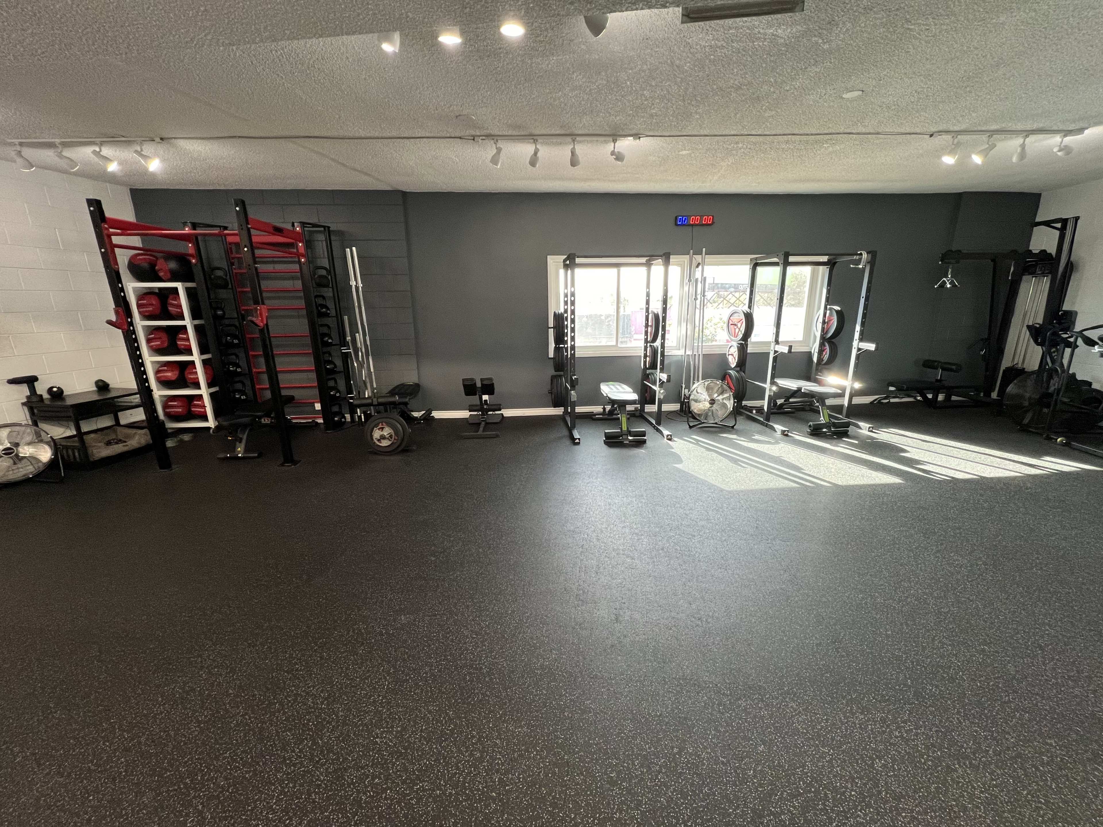 The image shows a fitness studio equipped with various exercise machines, weights, and open space for workouts.