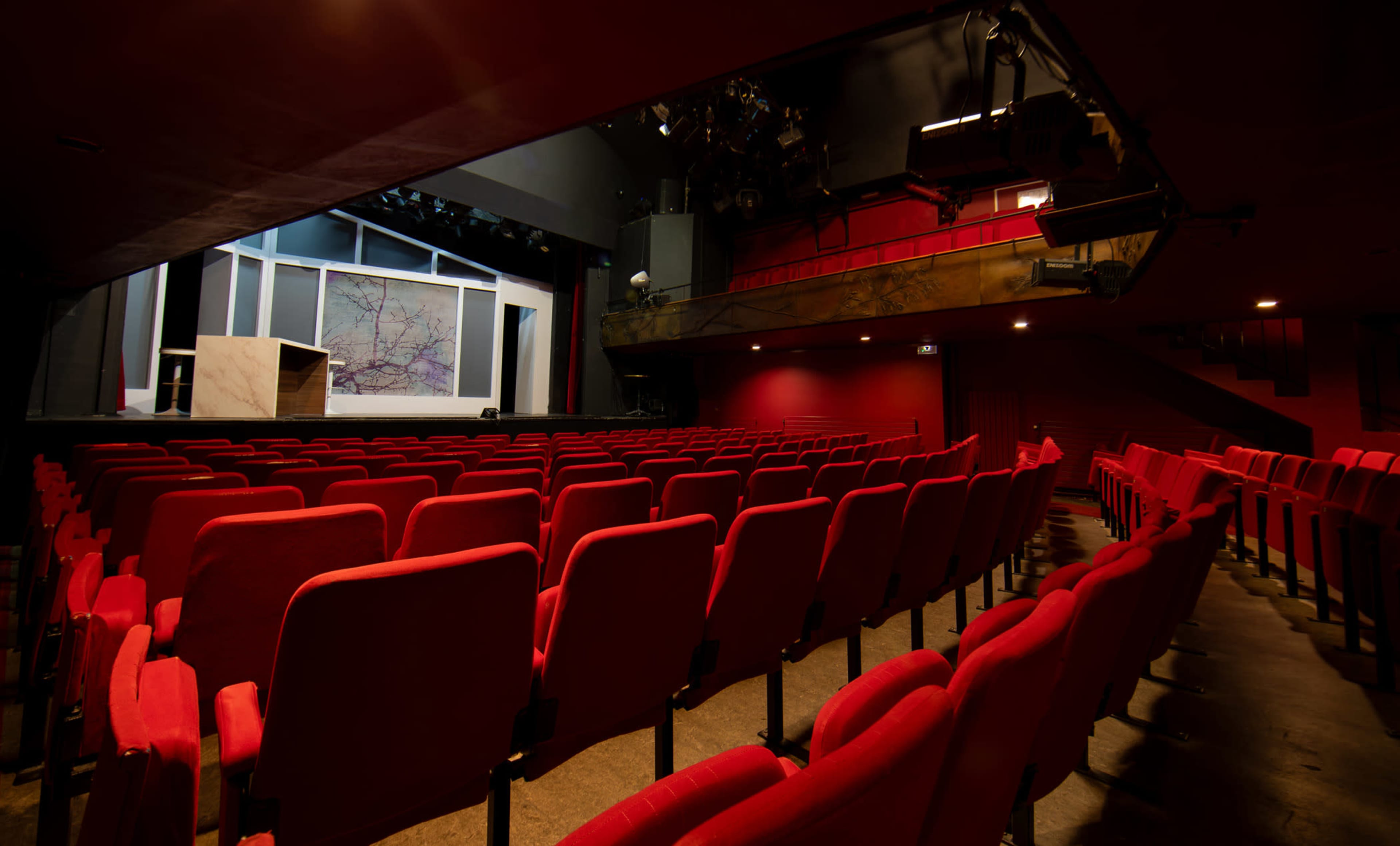 A theater with red seating arranged in rows facing a stage that features a backdrop and a podium.