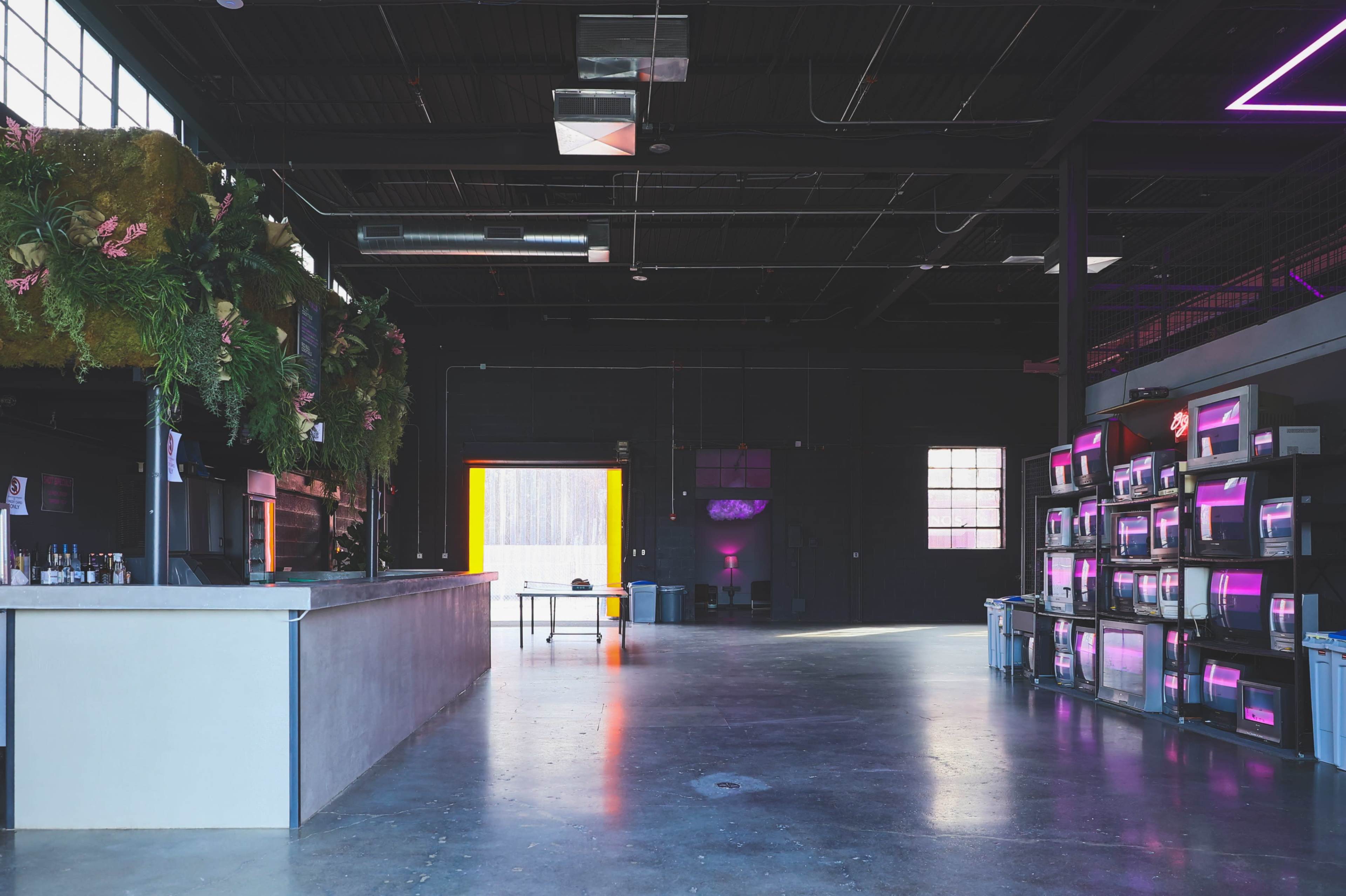 A spacious, modern interior of a bar with a concrete floor, a long counter, and shelves displaying decorative lights.