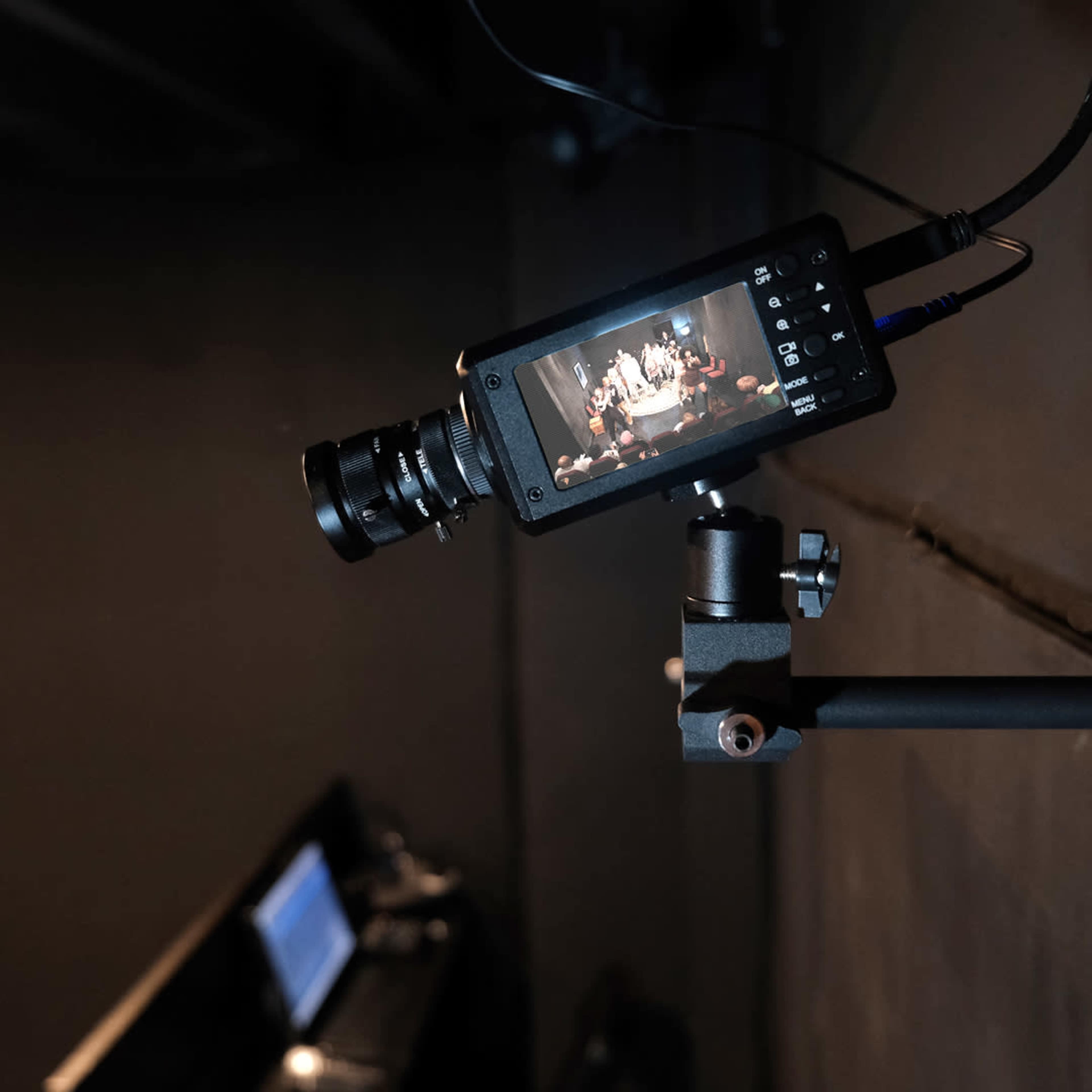 A camera is mounted on a stand, capturing a live event on its display, with a dark background.