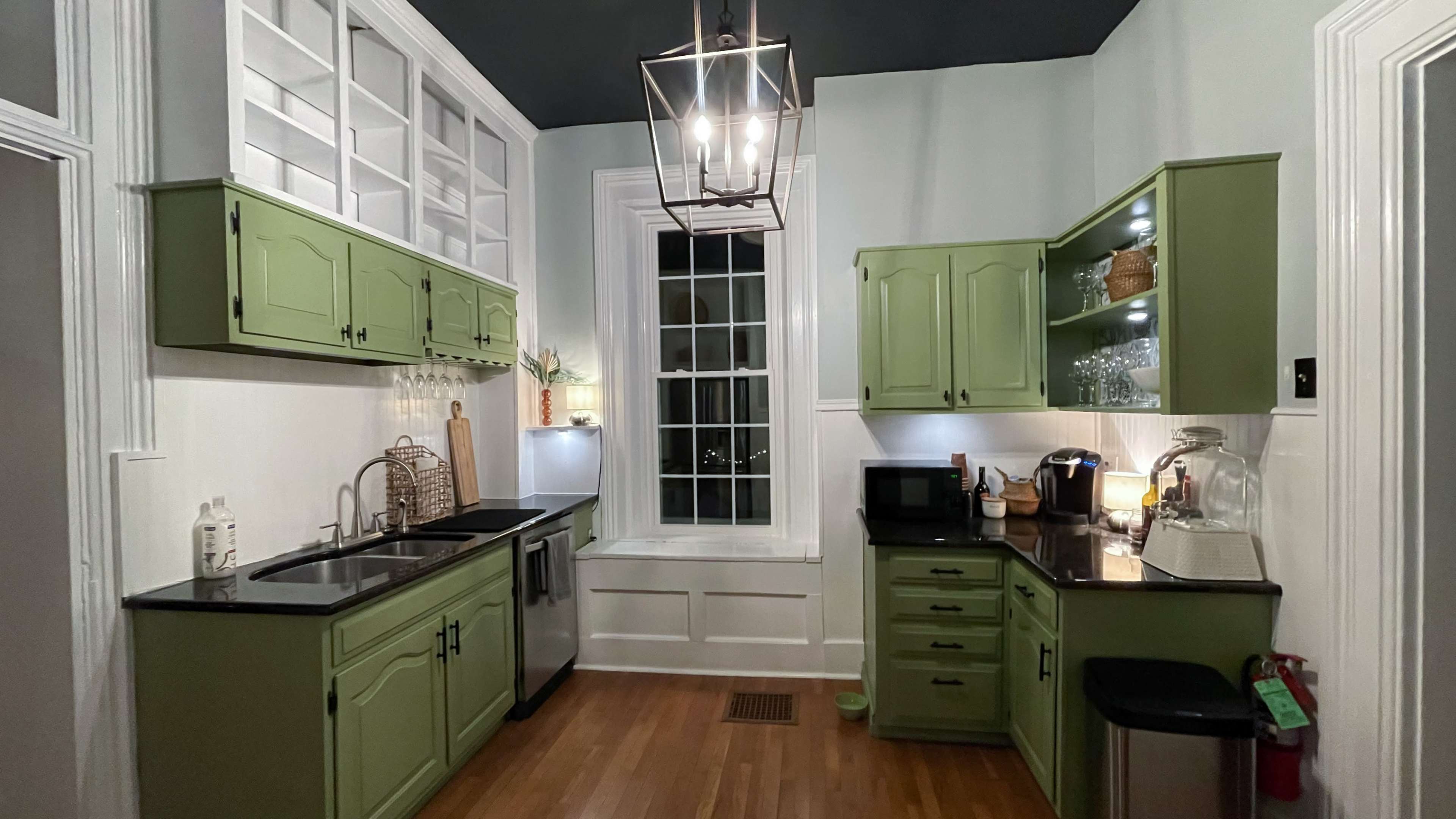 The kitchen features green cabinets, black countertops, a window with a view, and modern appliances.