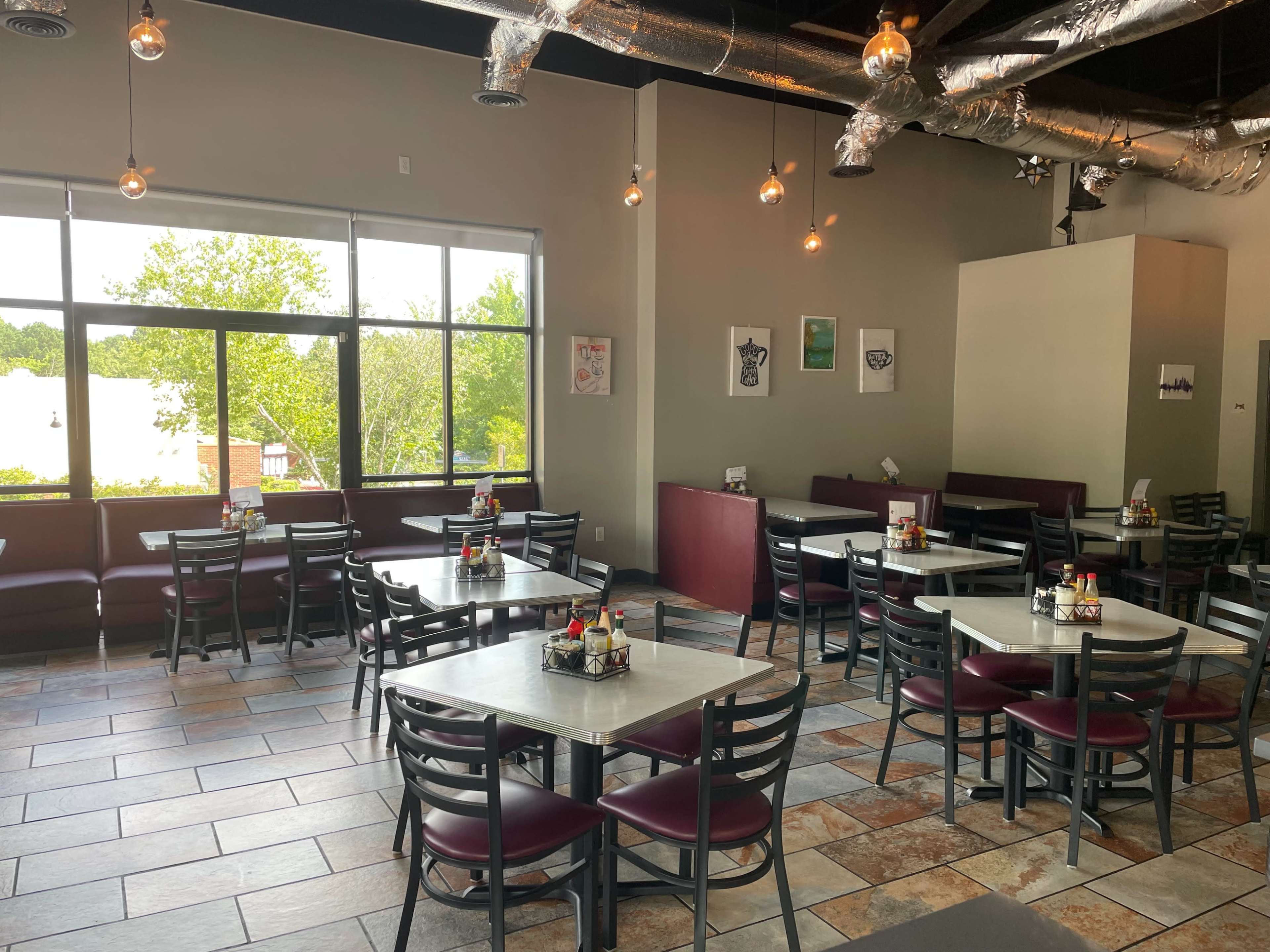 The image shows a dining area in a restaurant with several tables and chairs arranged near large windows.