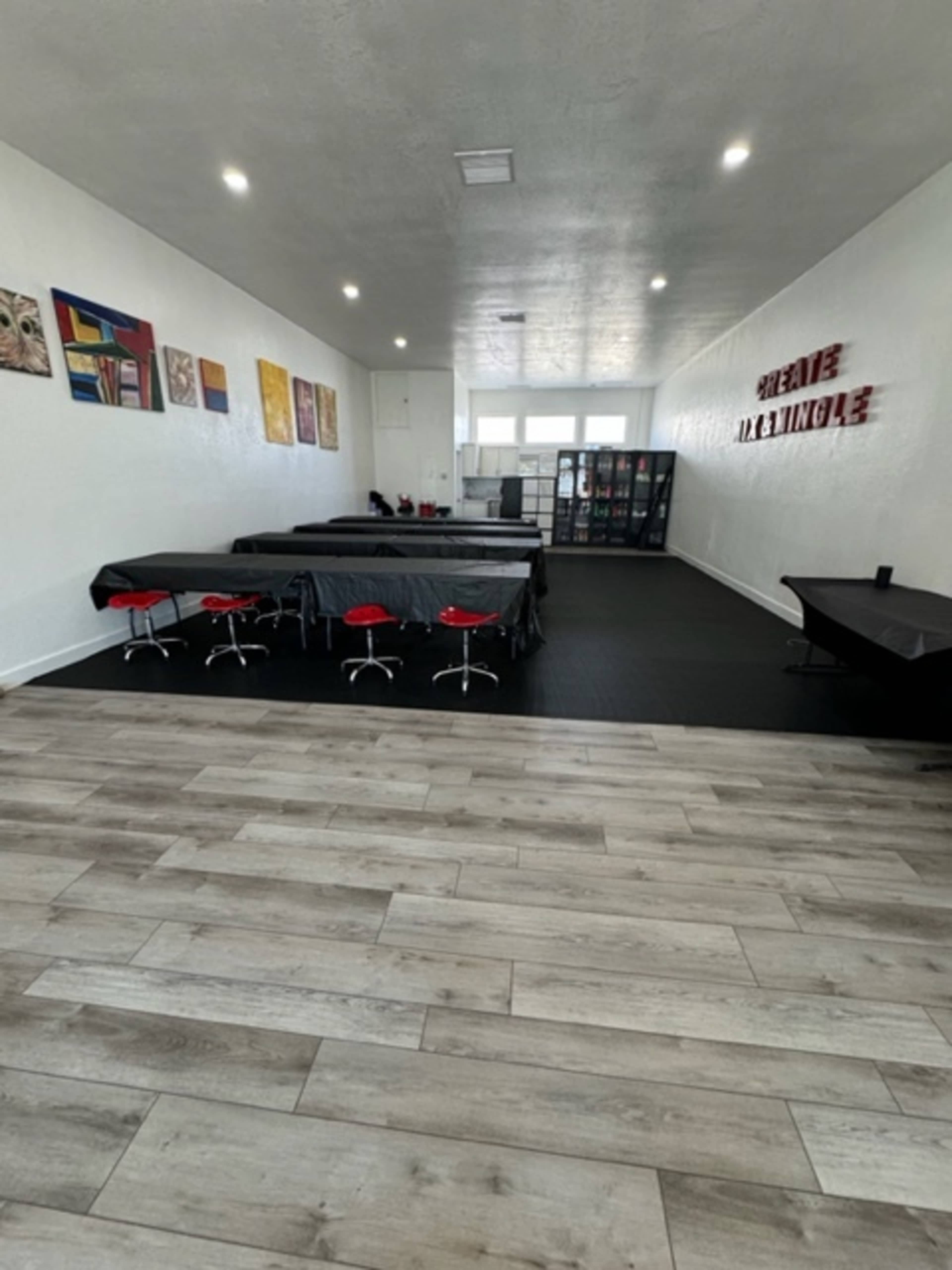 A spacious room with several tables covered in dark cloth, red stools, artwork on the walls, and vending machines in the background.