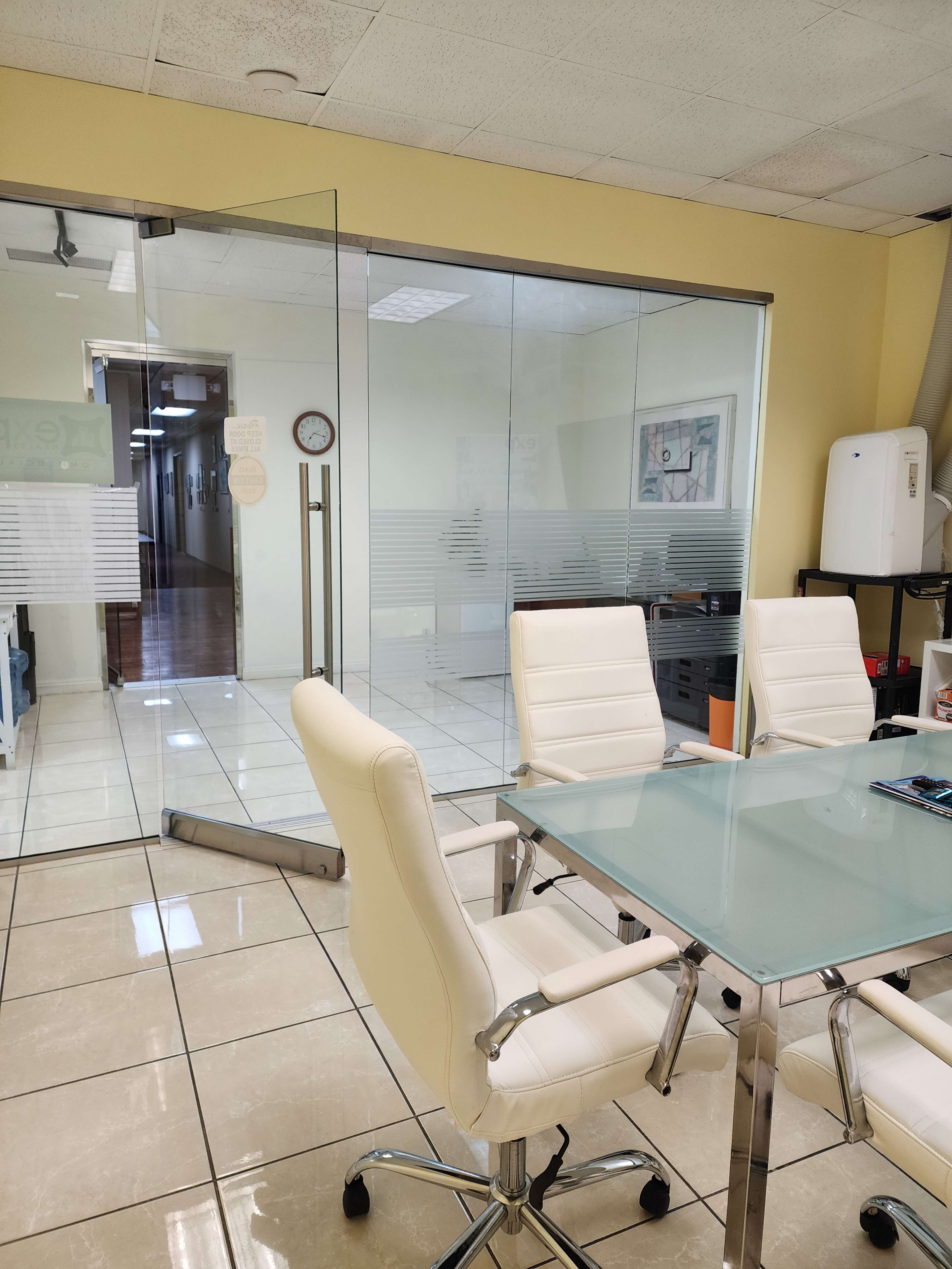 The image shows a modern conference room with a glass wall and white leather chairs surrounding a glass table.