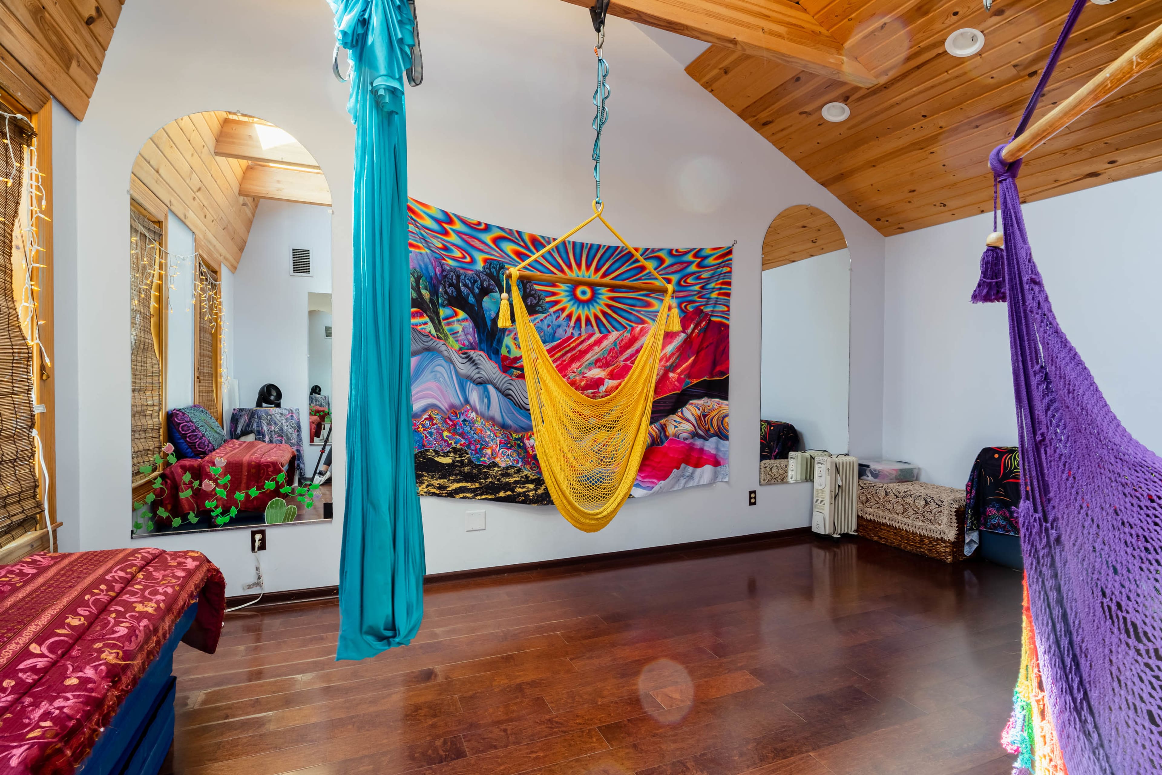A spacious room with wooden ceilings, featuring vibrant wall art and two hanging hammocks.