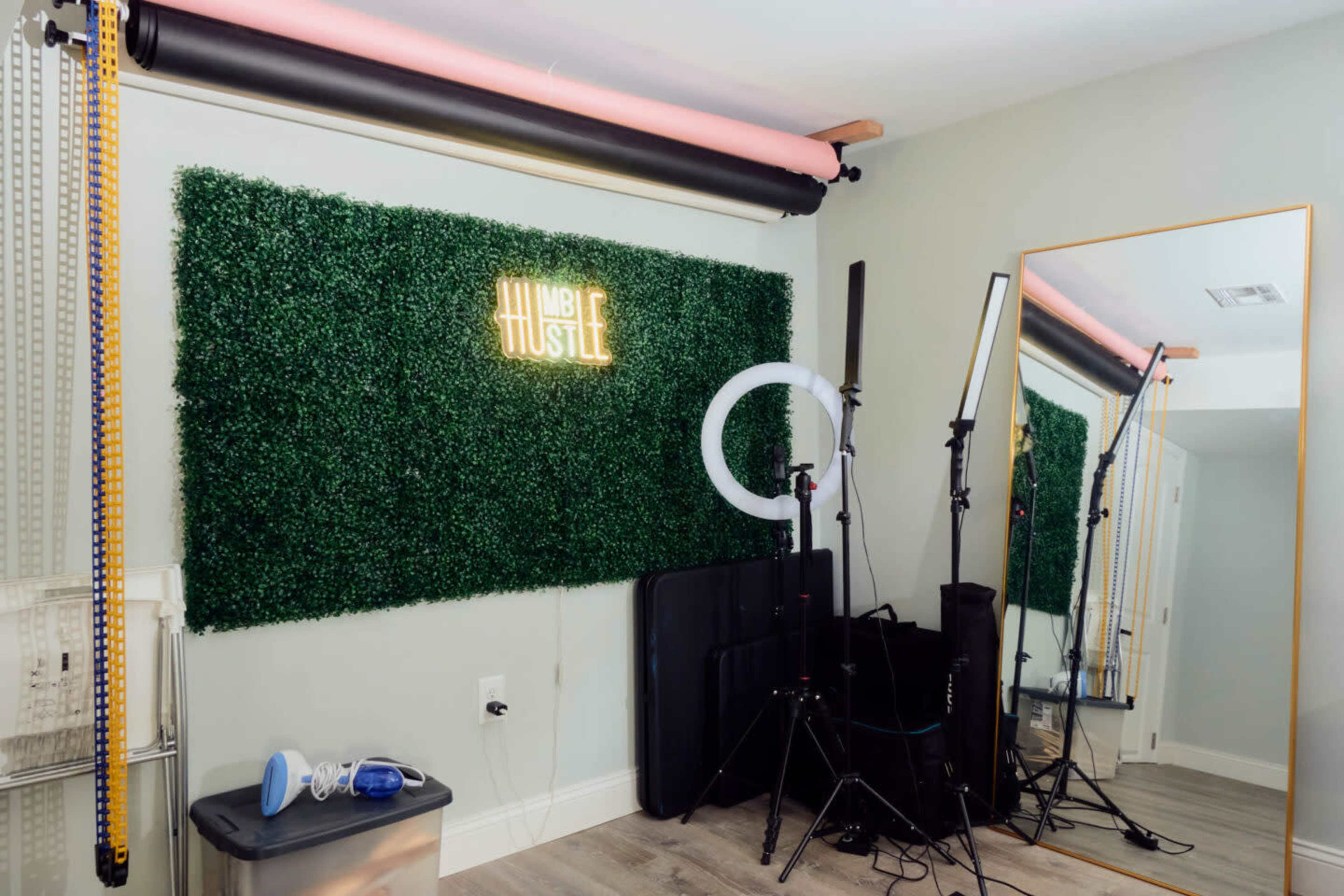 A room with a green grass wall, a mirror, and lighting equipment set up for photography or video production.