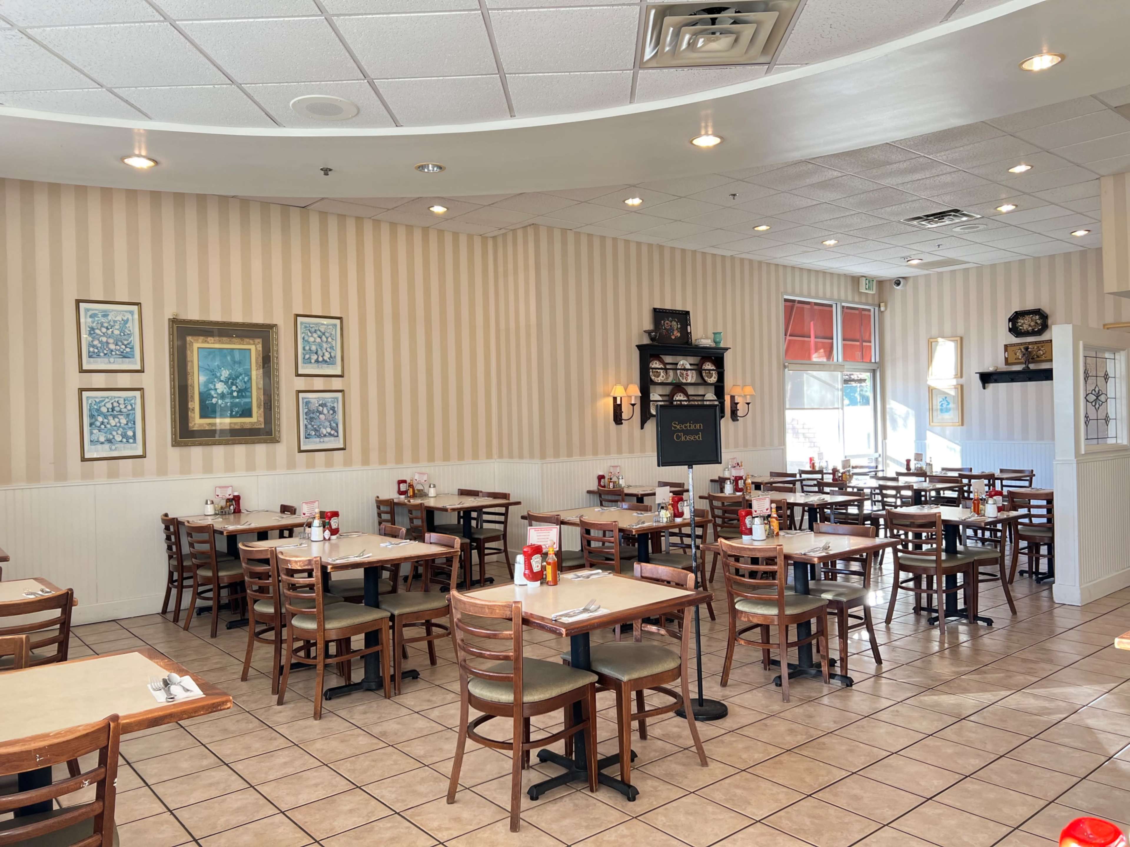The image shows the interior of a restaurant with rows of tables and chairs, light-colored walls, and framed artwork.