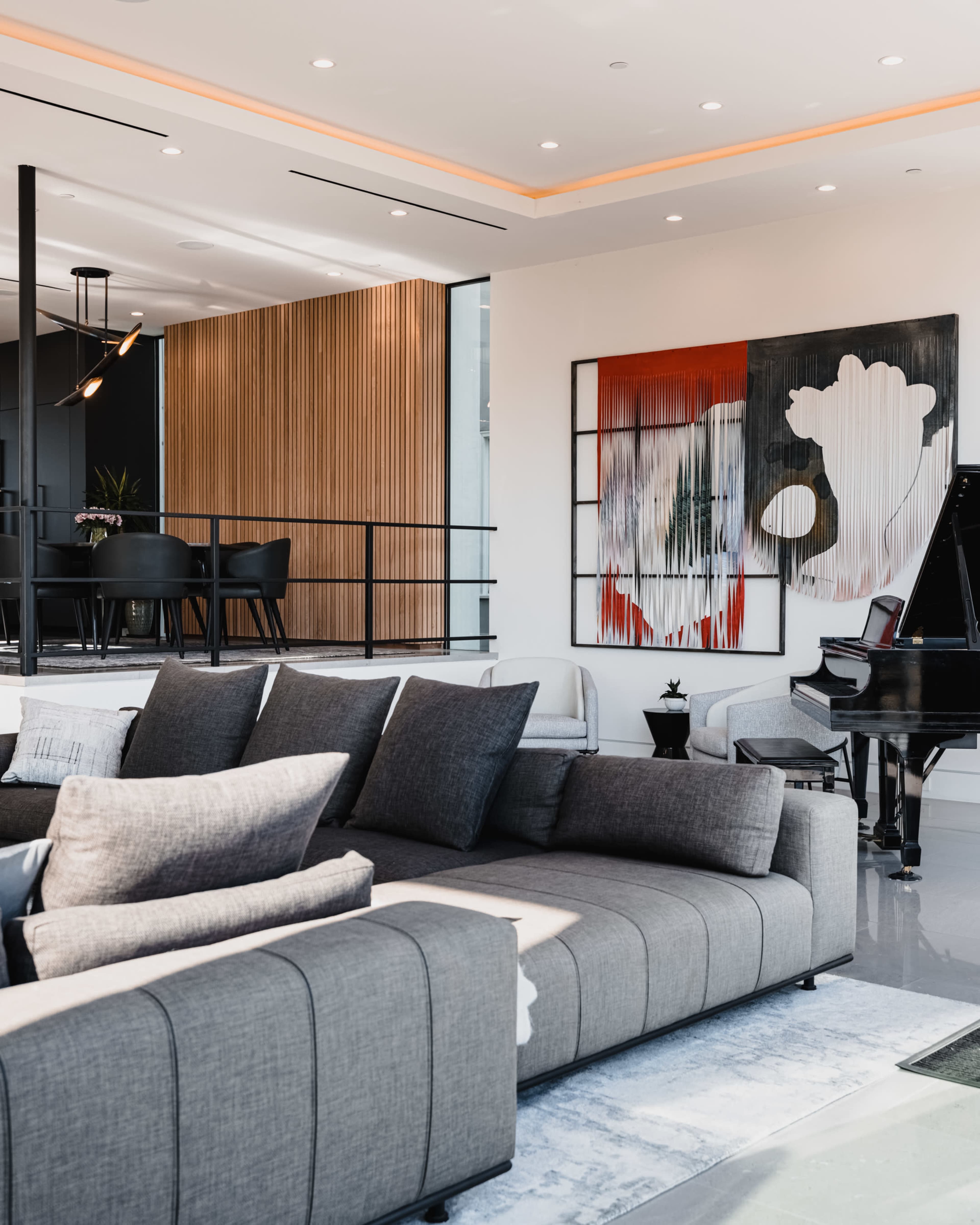 A modern living room features a gray sectional sofa, a black grand piano, and a large abstract painting on the wall.