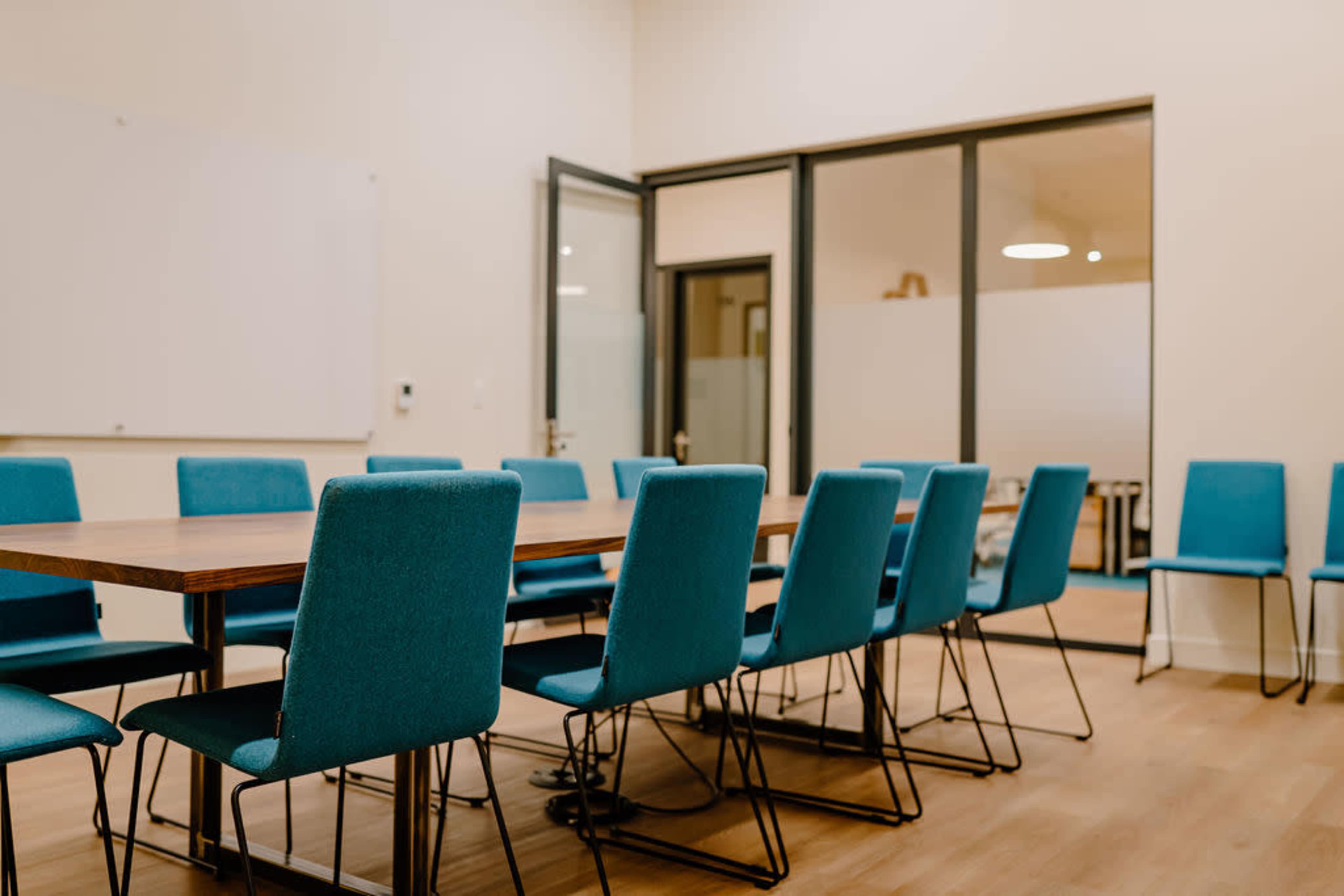 A large conference room features a long wooden table surrounded by blue upholstered chairs.