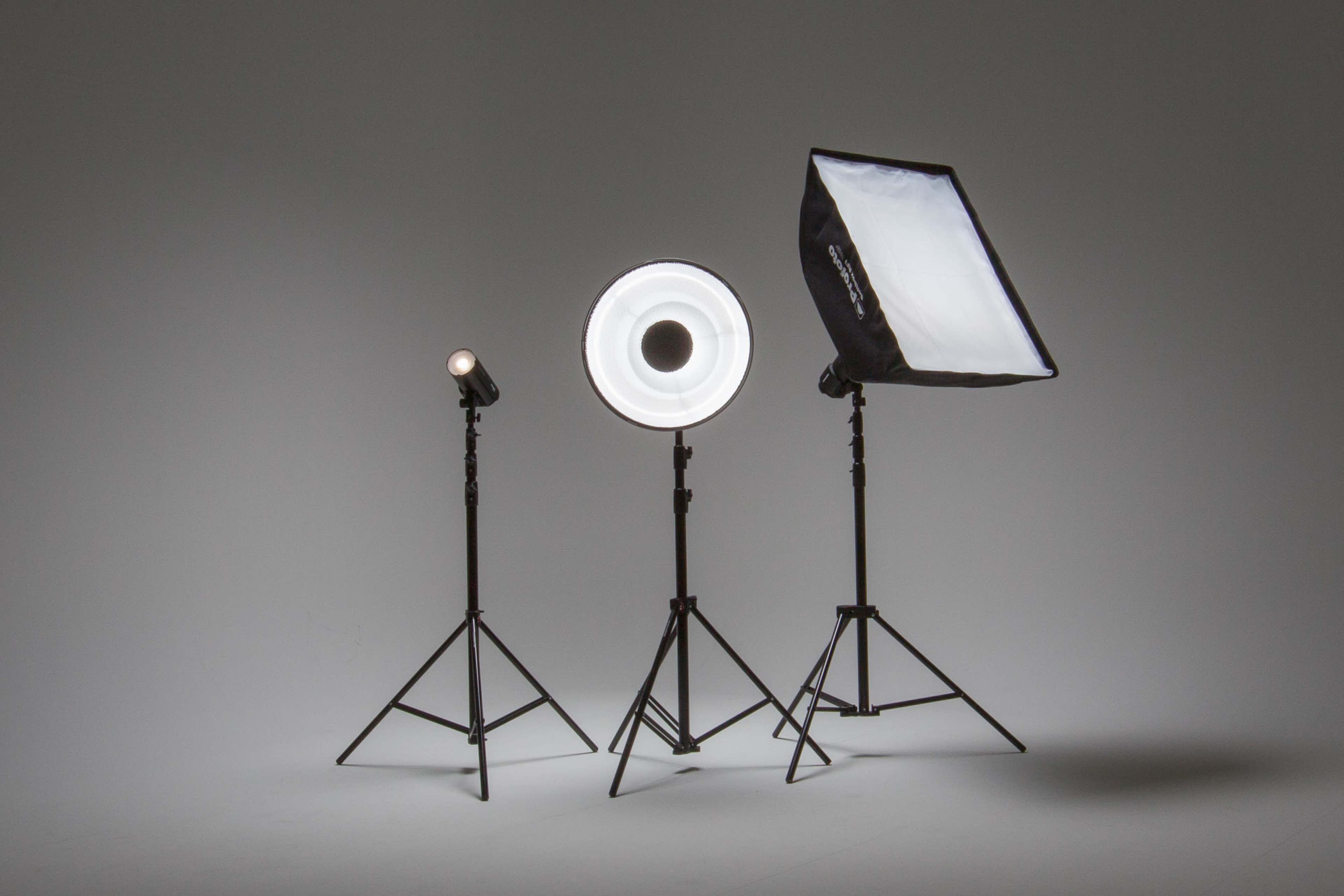 Three photography light fixtures on adjustable stands against a plain gray backdrop.