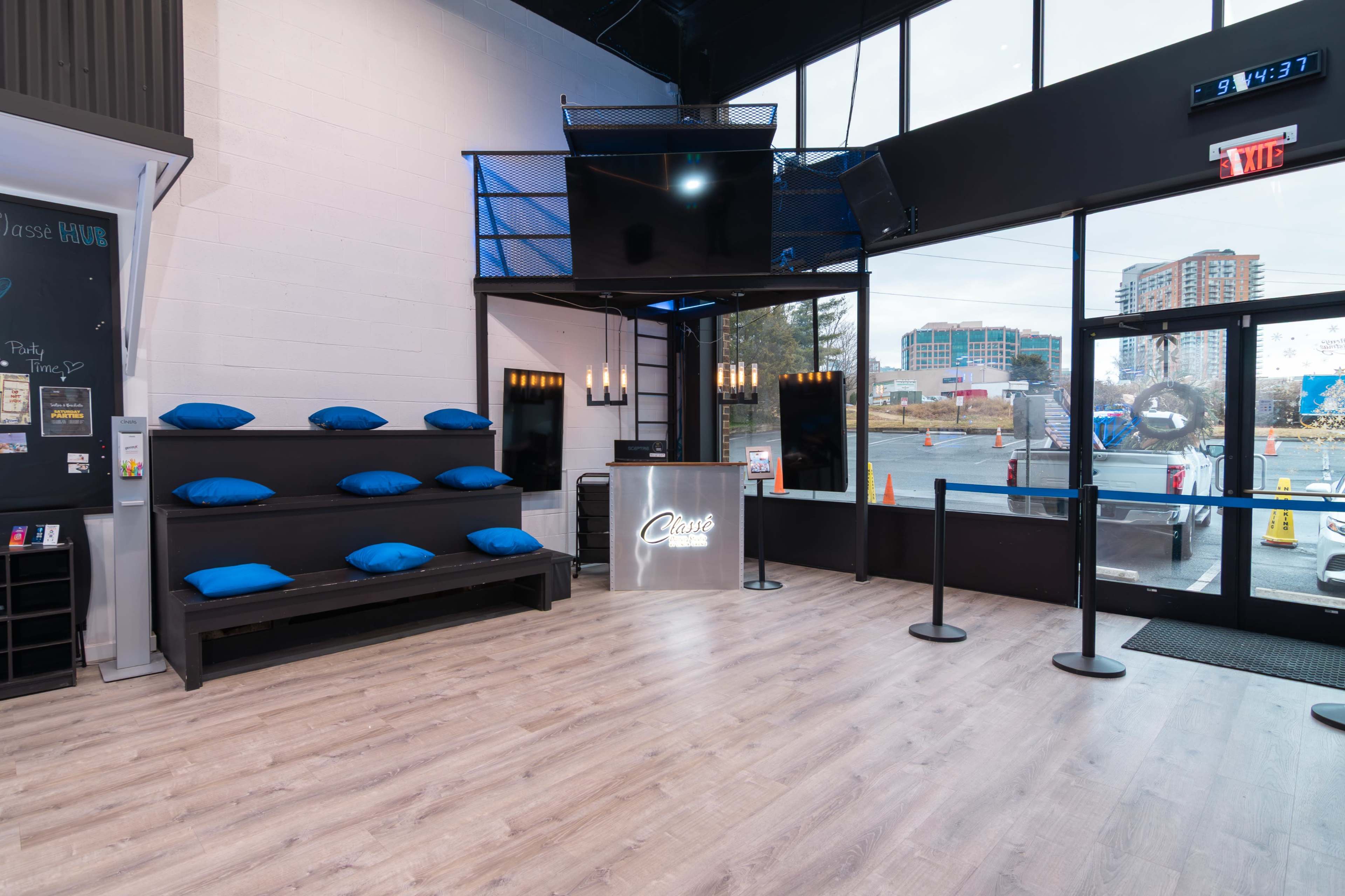 The image shows a modern reception area with a sleek counter, blue pillows on a black platform, and large windows providing a view of the outside landscape.