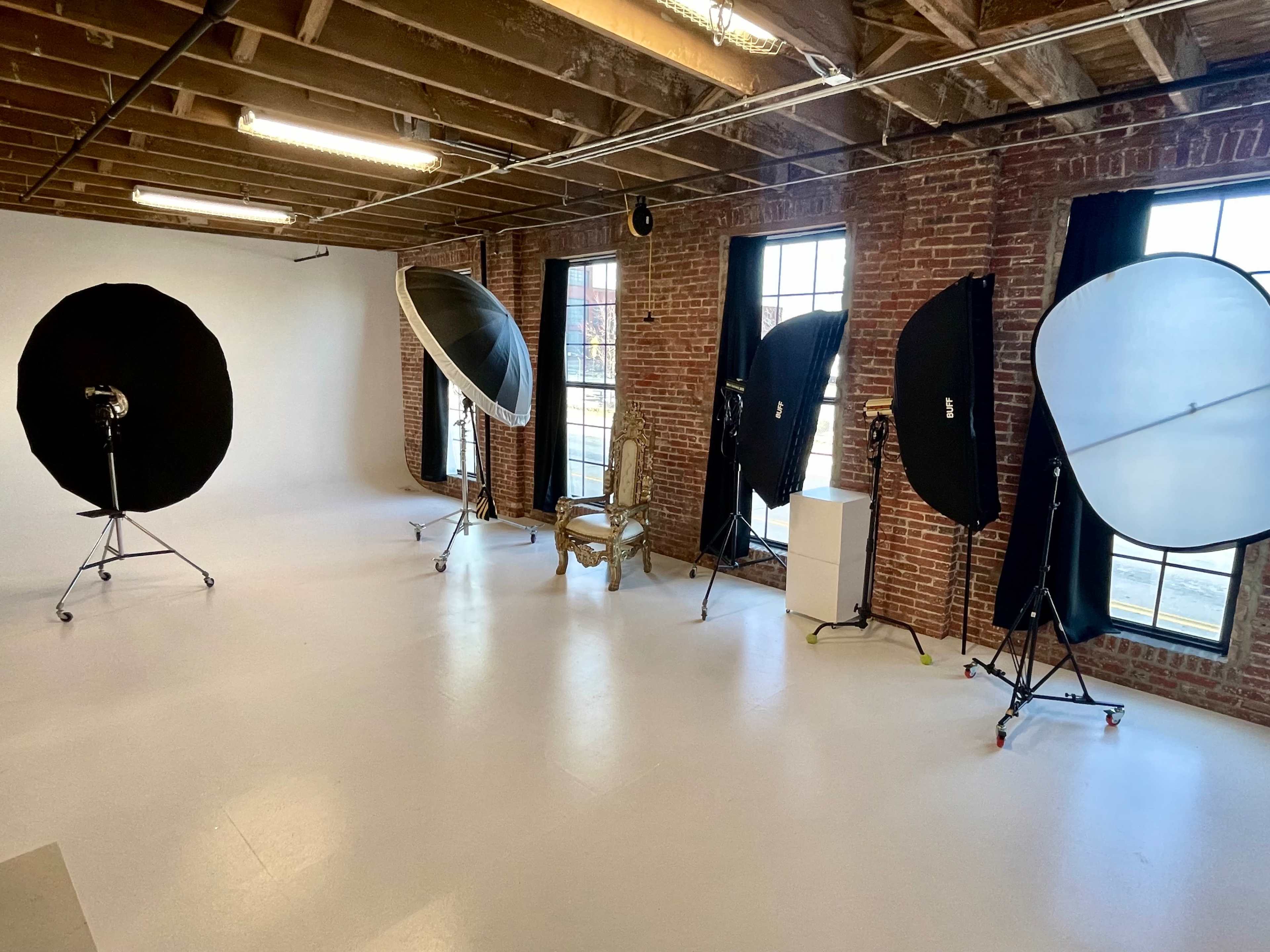 A photography studio with softboxes on stands, a vintage chair, and large windows allowing natural light.