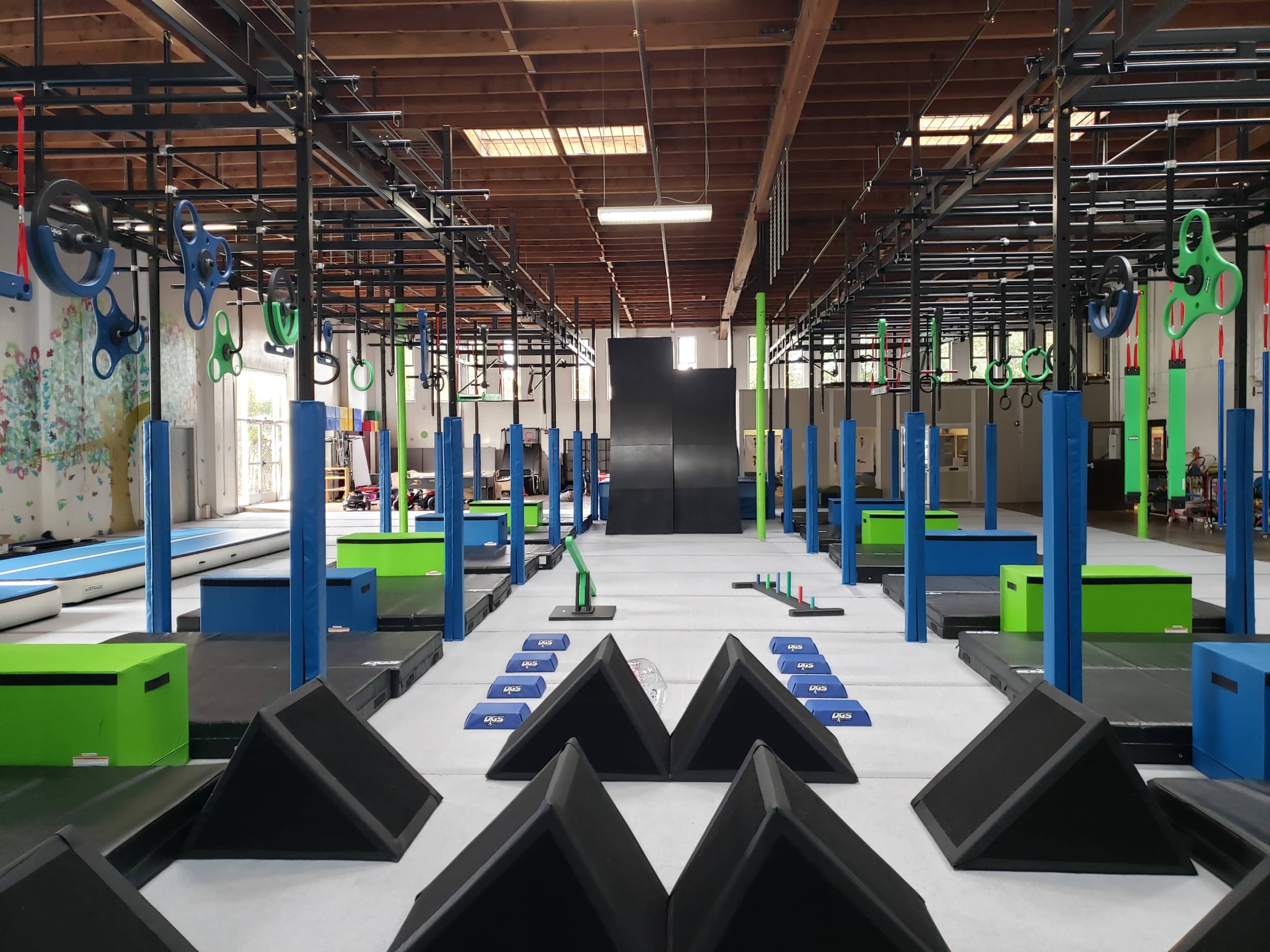 An indoor training facility featuring various fitness equipment, including climbing walls, mats, and reaction training structures arranged in rows.
