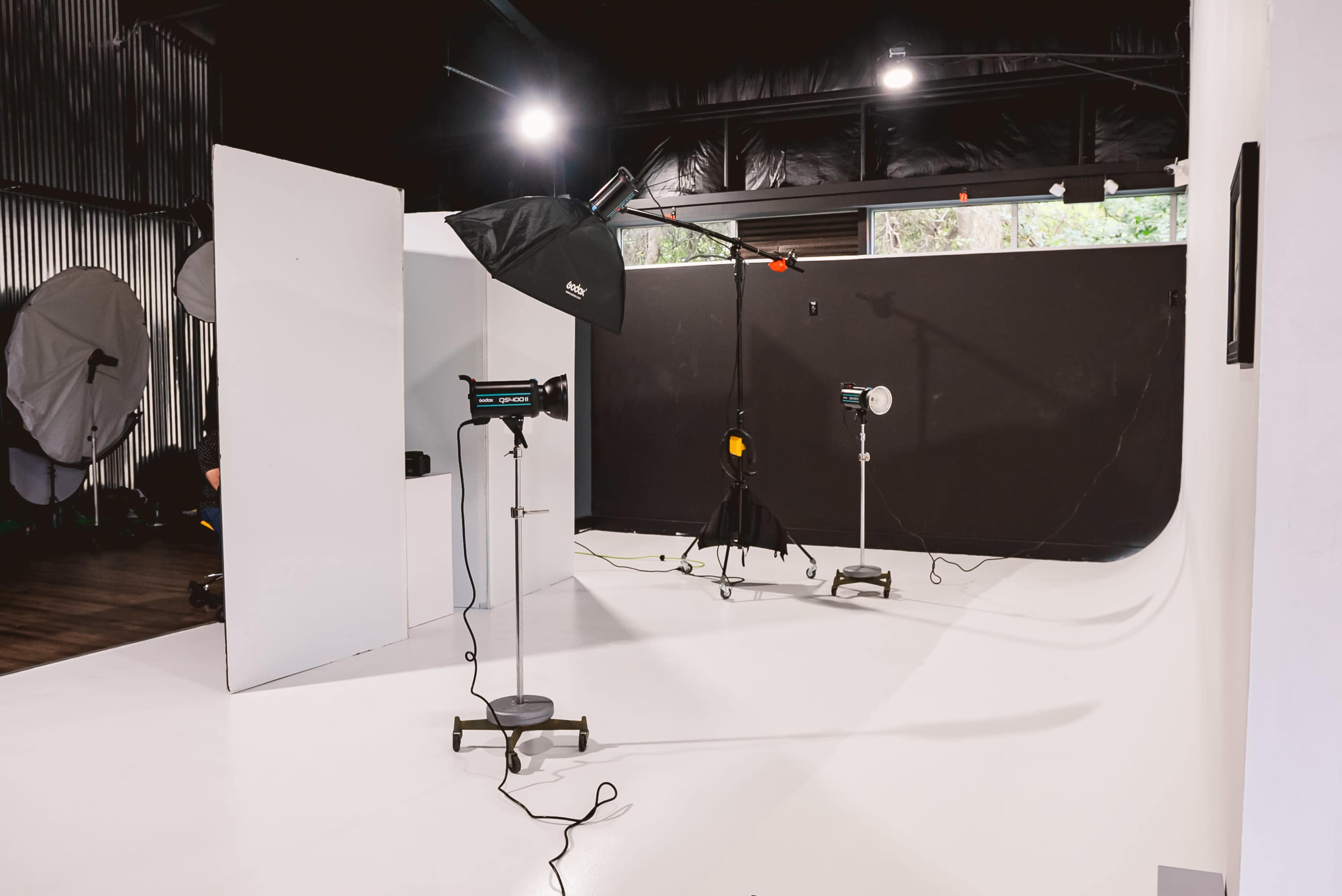 A photography studio is set up with various lighting equipment and backdrops, featuring a white wall and a black backdrop.