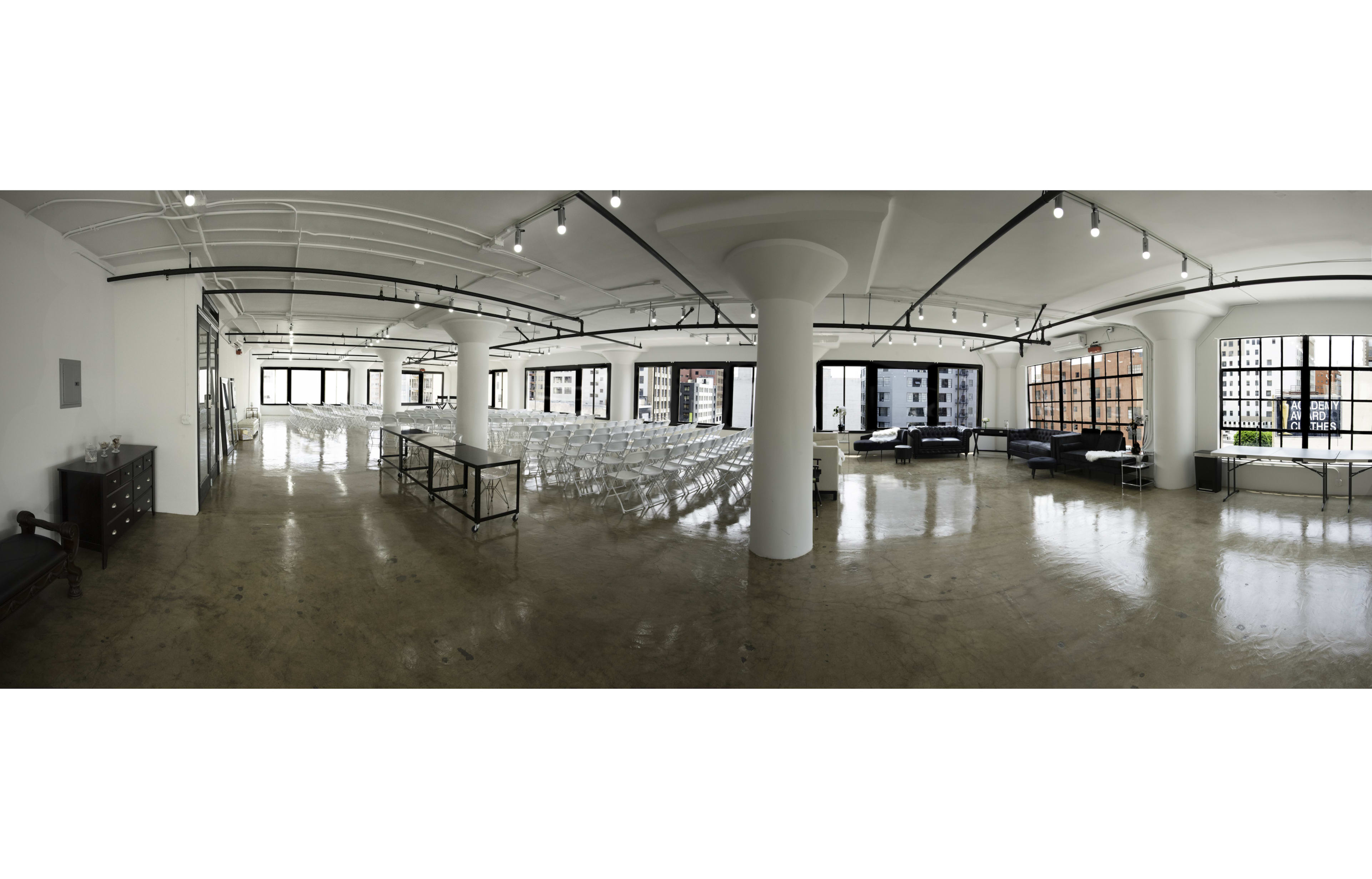 The image shows a spacious, empty event venue with rows of chairs set up, large windows, and a polished concrete floor.