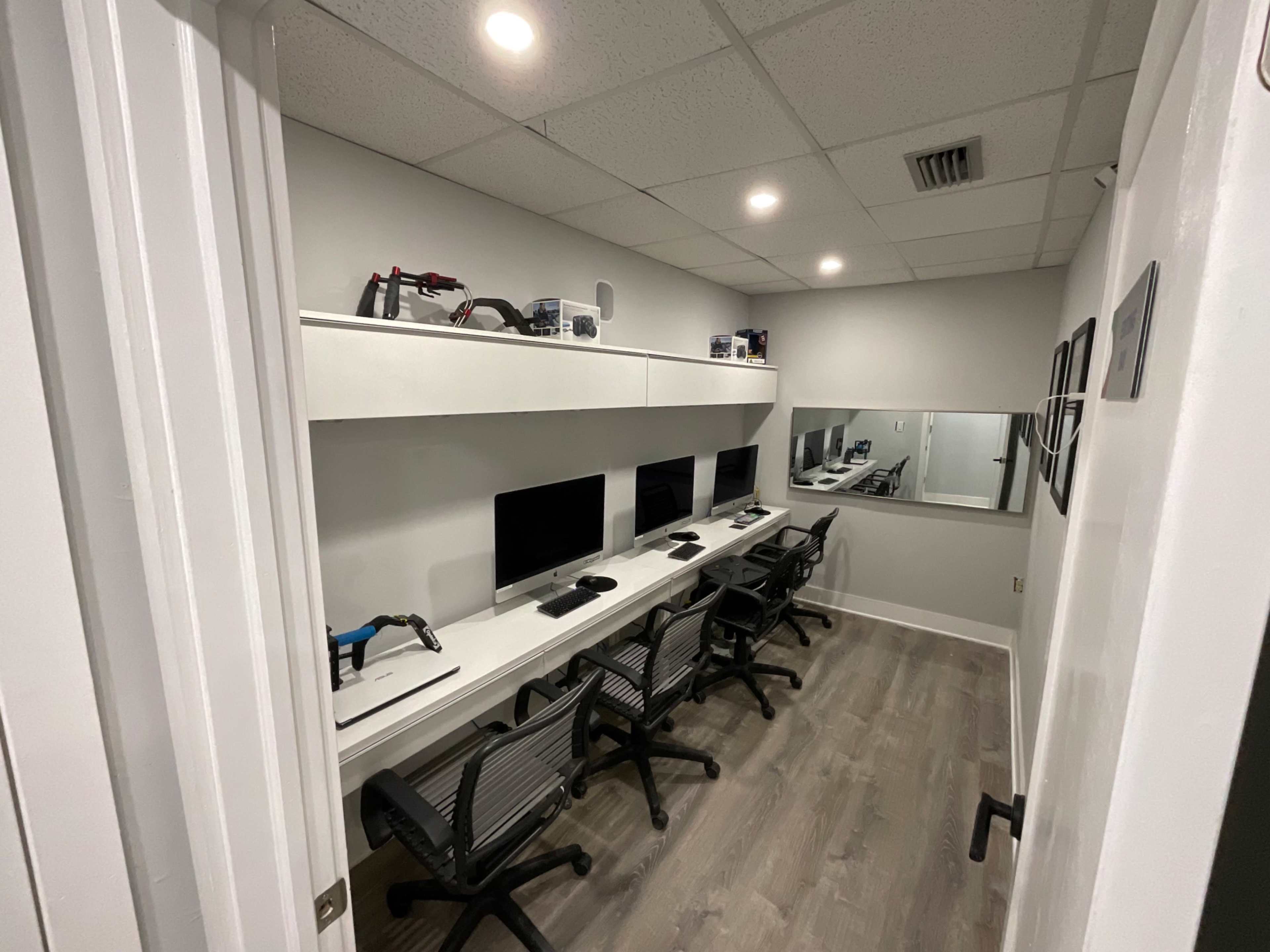 A minimalist office space with four computers arranged on a white desk, along with tools and a mirror on the wall.