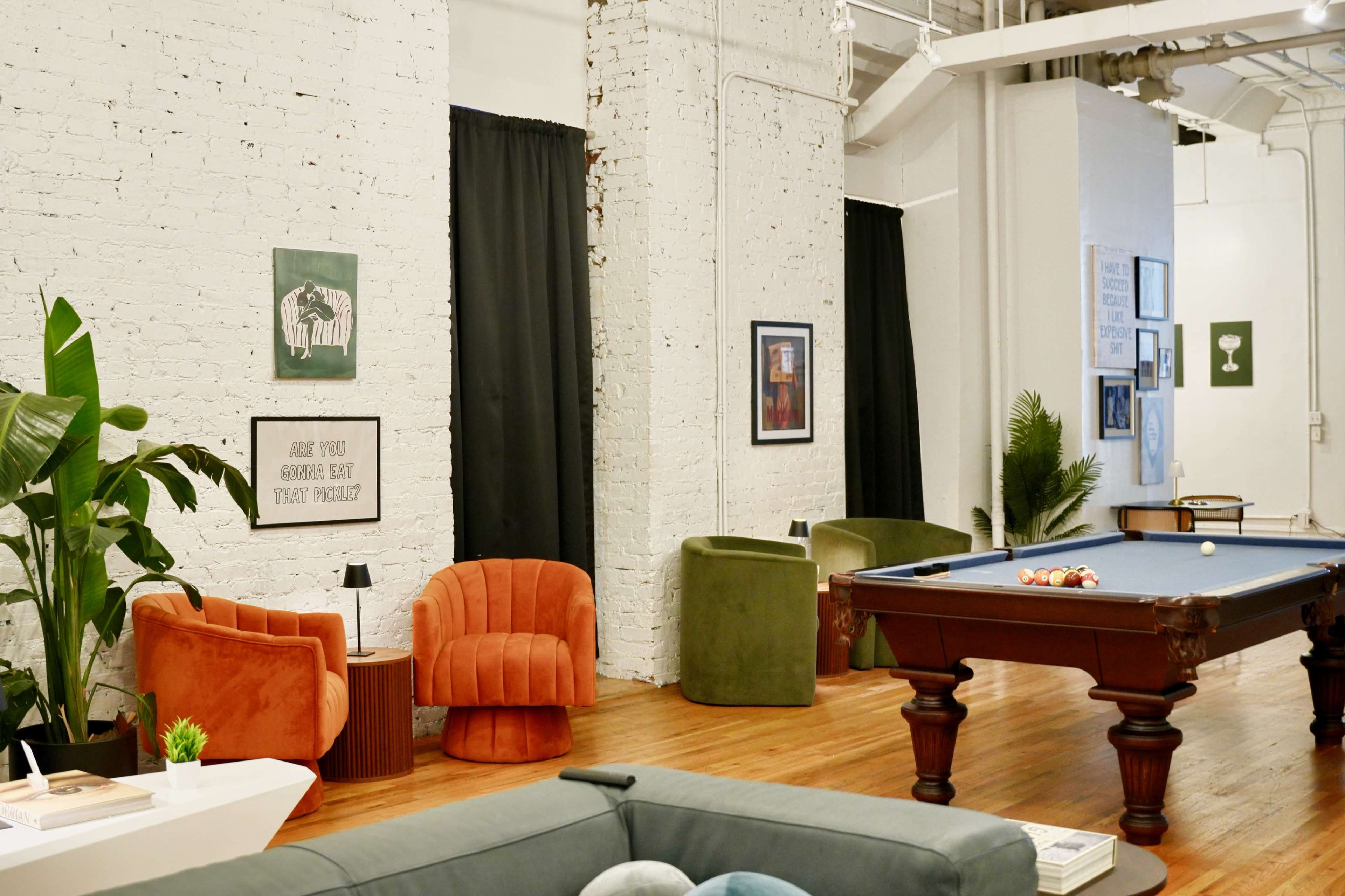 The image shows a spacious interior featuring a billiard table, colorful seating areas, and decorative wall art against white brick walls.